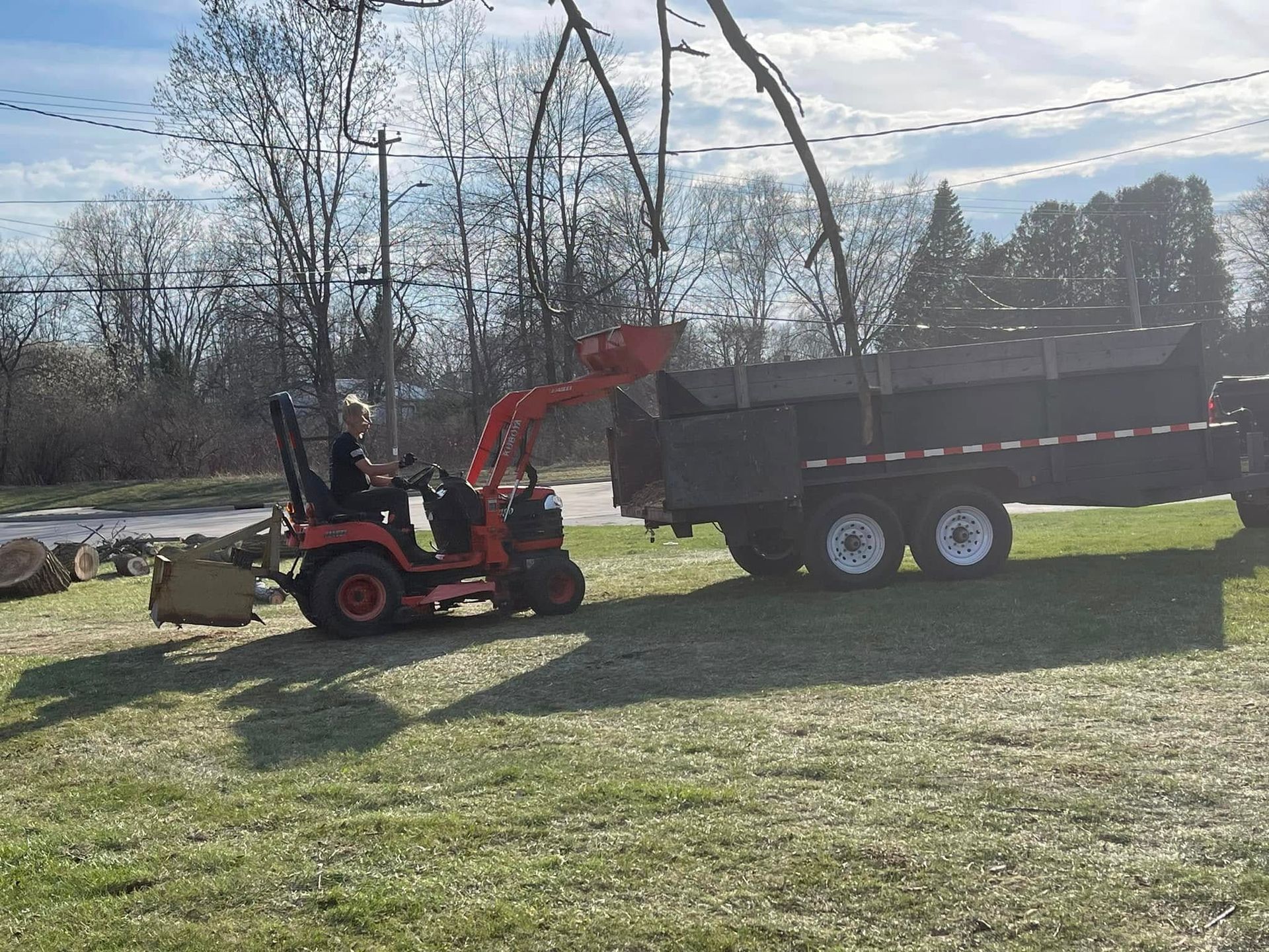 Red tractor loading dirt into a black dump trailer in a sunny field