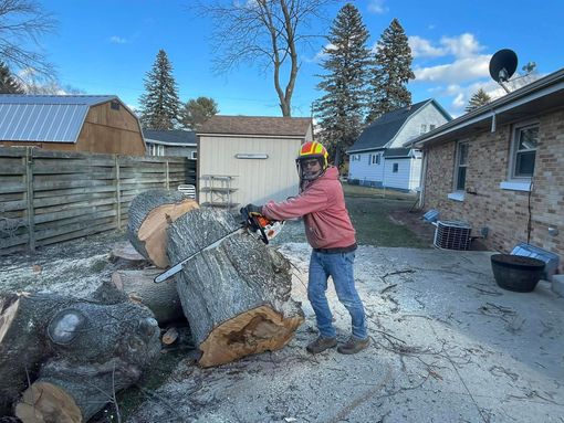 Utility truck lifting a tree branch near a snowy house and parked car during winter