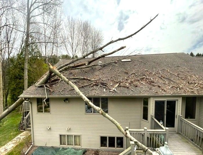 Fallen tree branch damaged the roof of a beige house, with debris scattered on top.