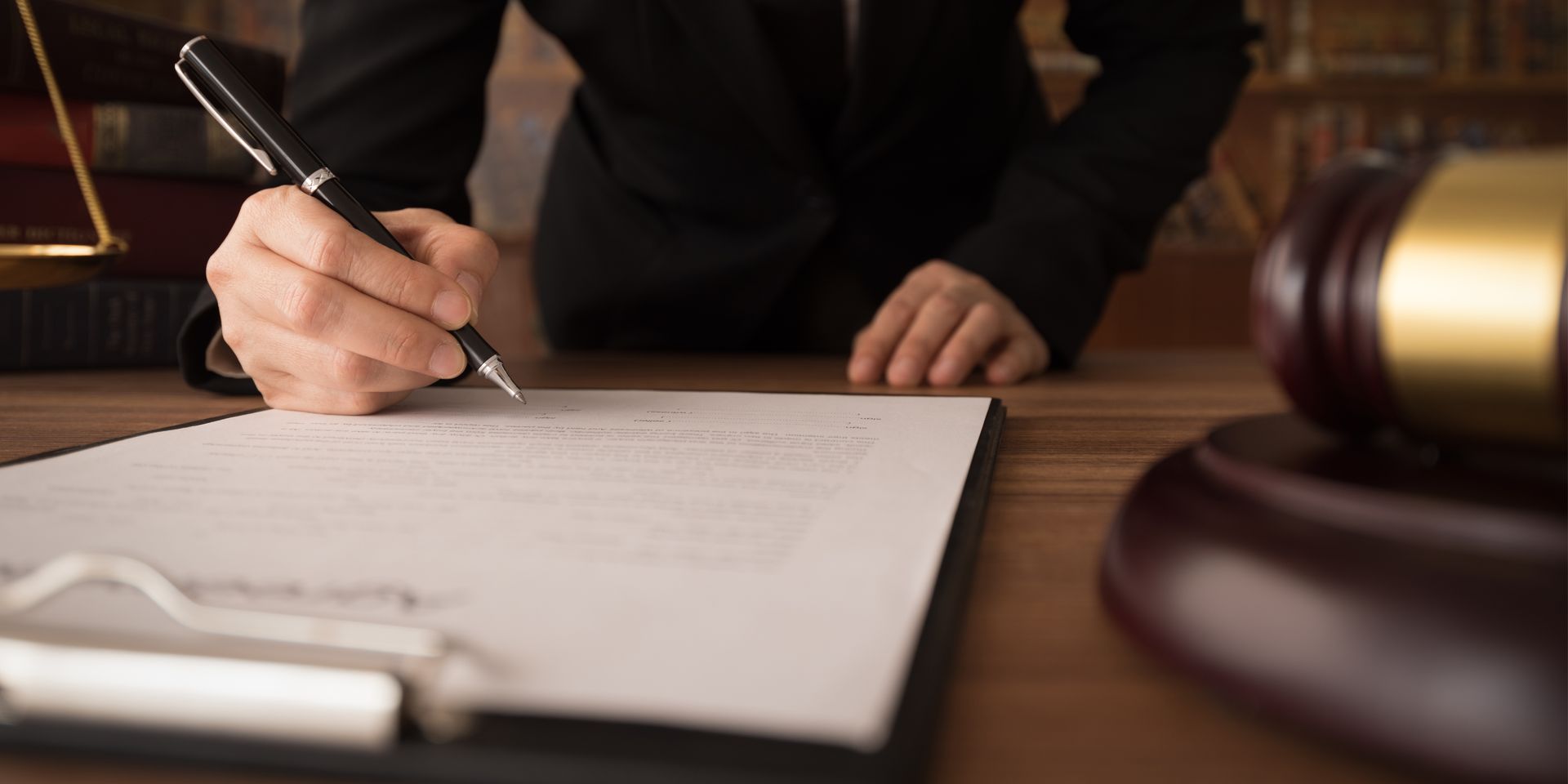 A person is signing a document on a clipboard with a pen.