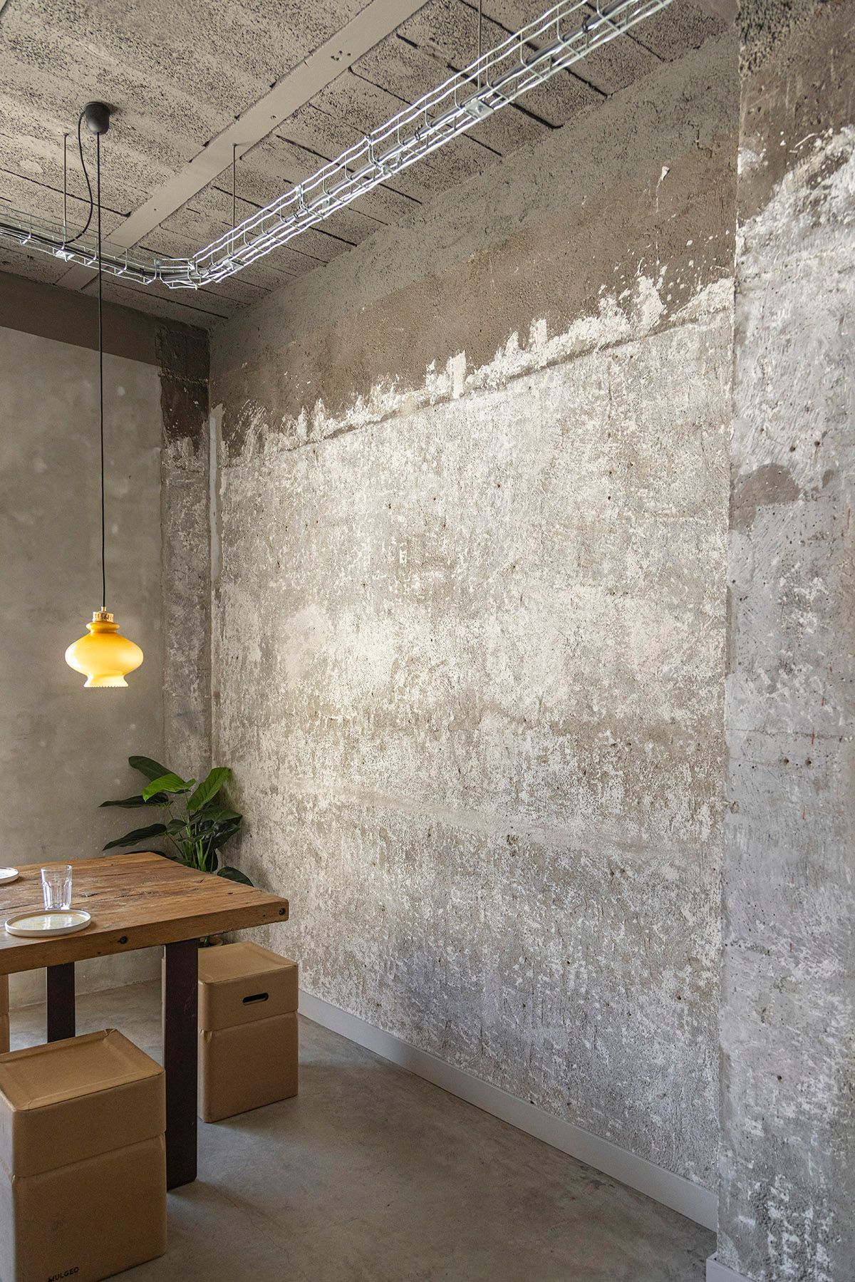 Fotografia Emfasi Estudi Andorra. Un comedor con mesa y sillas frente a un muro de concreto.