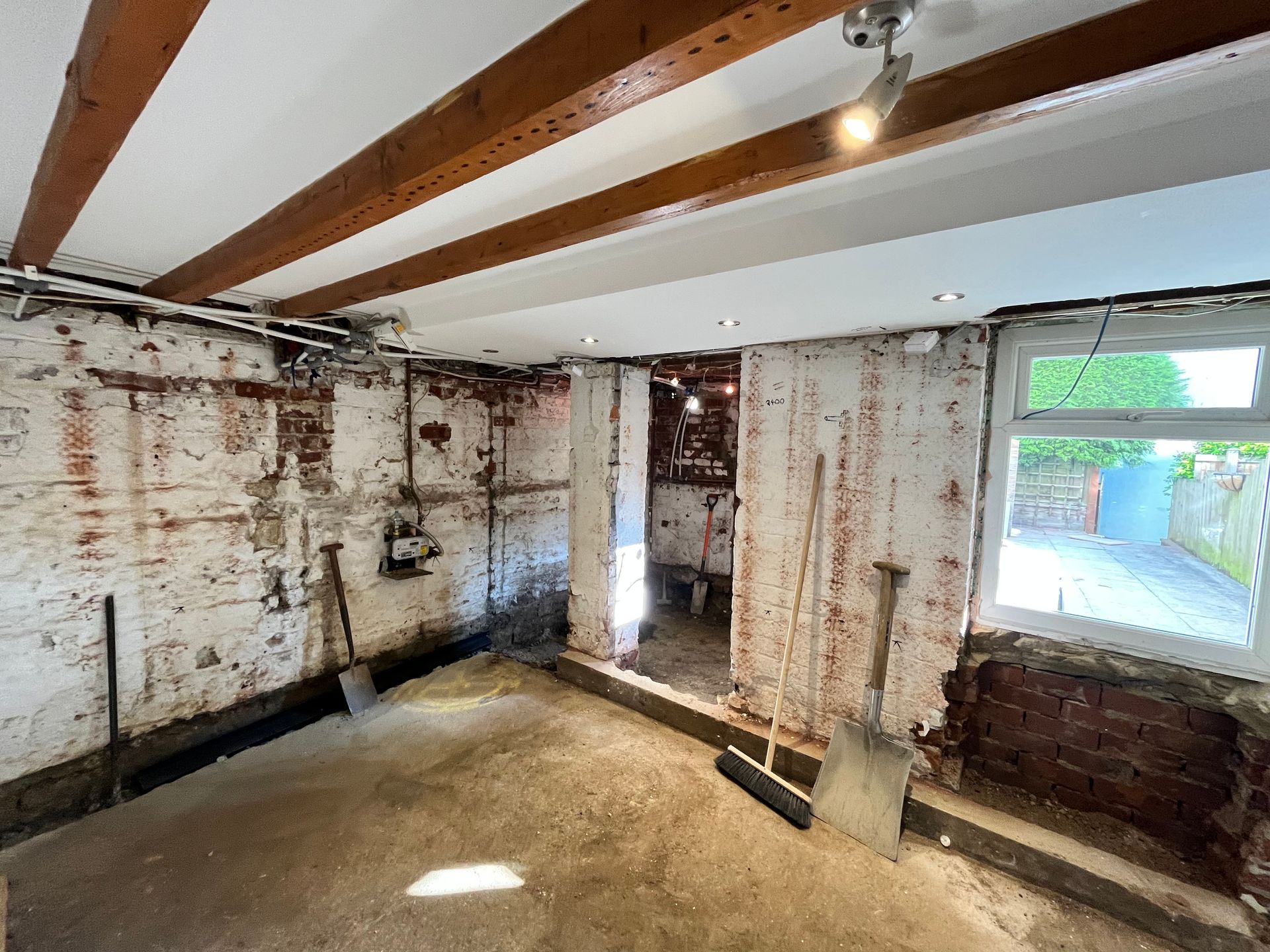 Renovated basement with exposed brick walls, beams, and concrete floor. Light streams in through a window.