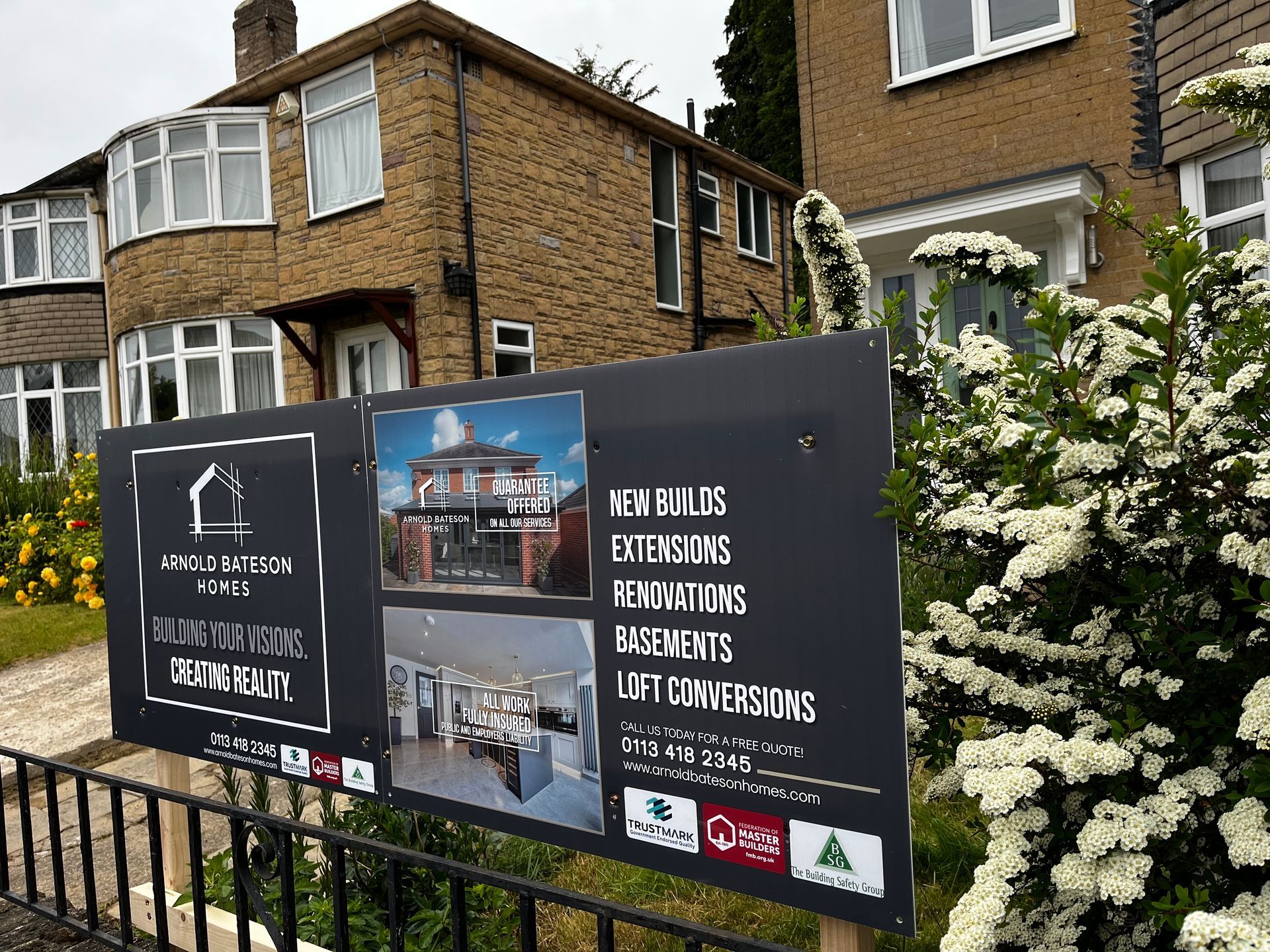Sign advertising construction services in front of a stone house with an obscured view.