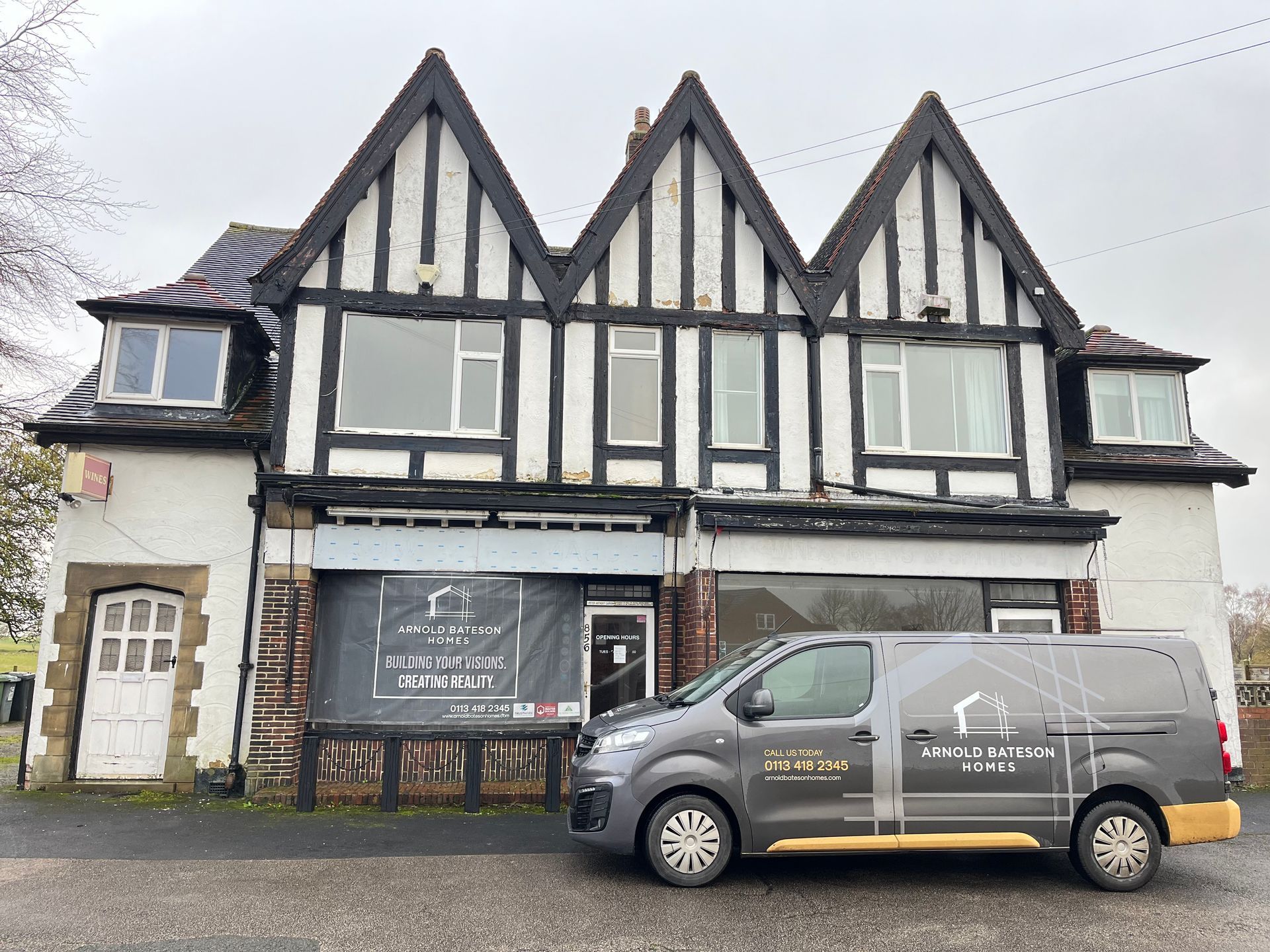 Tudor-style building with a company van parked in front. The building has a sign and boarded-up windows.