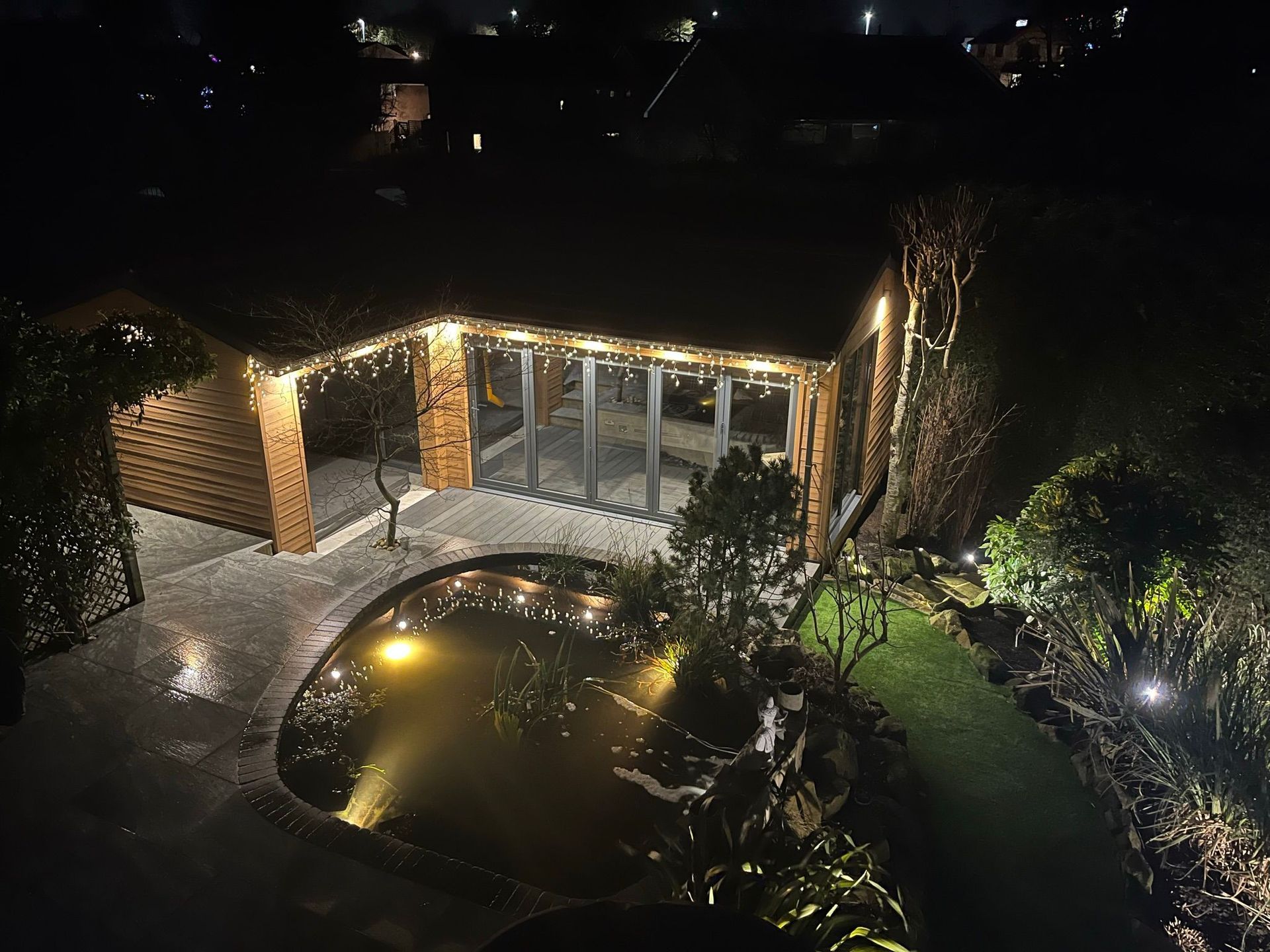 Wooden building and pond illuminated at night with string lights.