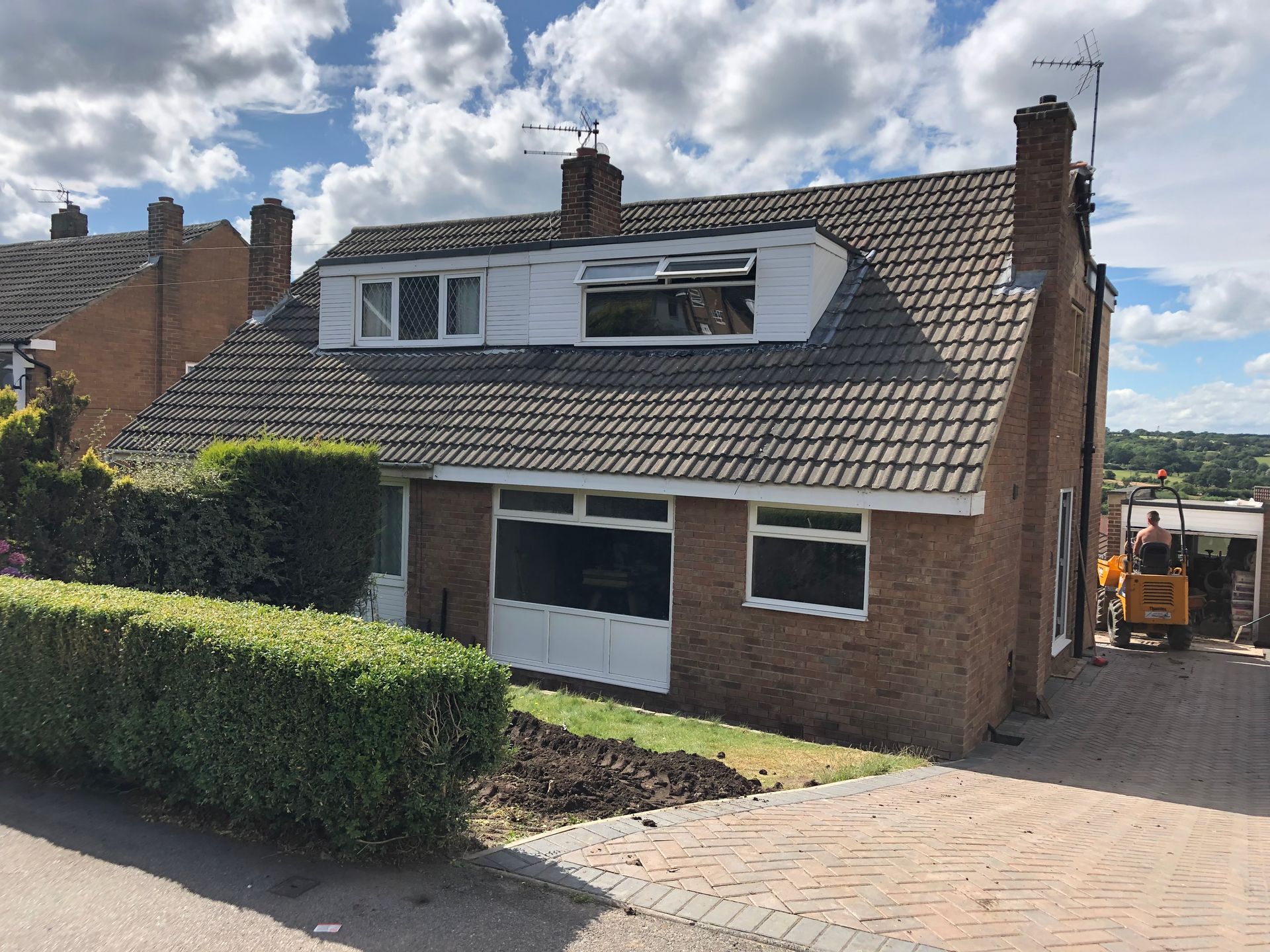 Brick house with a dormer, two chimneys, and a paved driveway.
