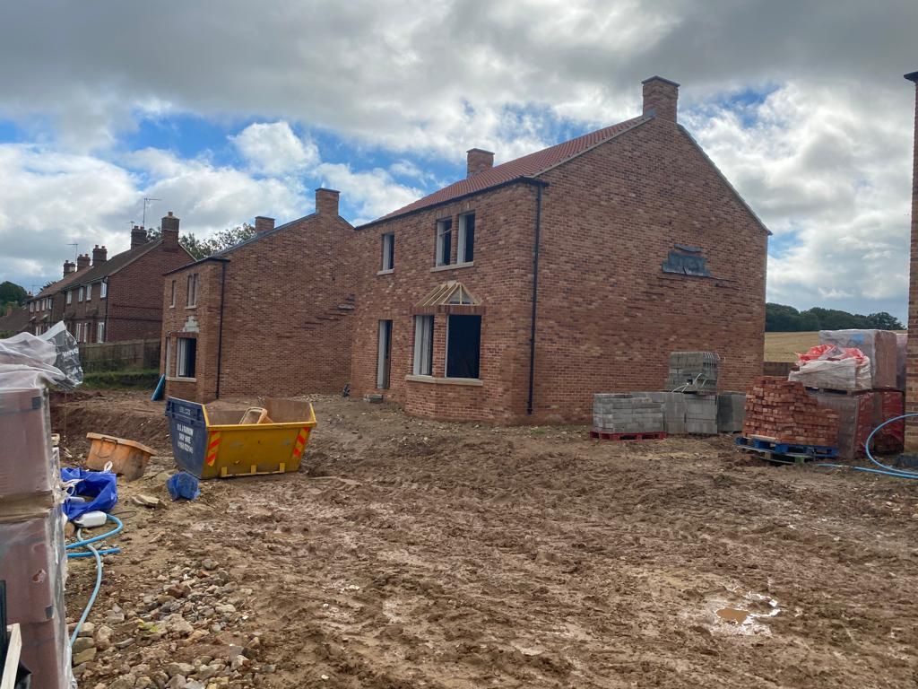 Brick house under construction with muddy ground and construction materials.