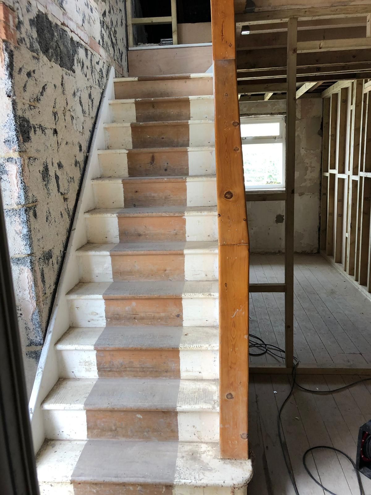 Staircase under construction: wood steps alternating brown and white, wooden banister, unfinished walls.