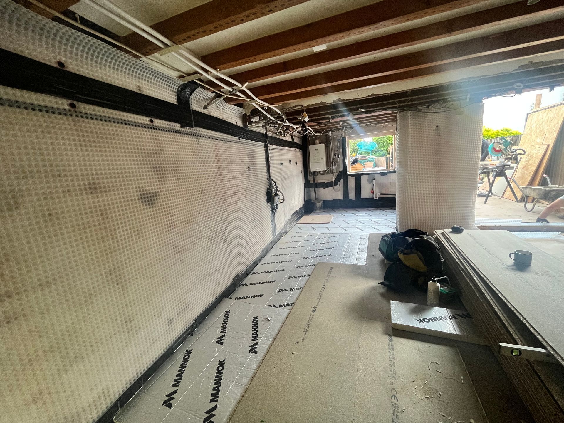 Interior view of a basement under construction with a drainage membrane on walls and floor; exposed beams.