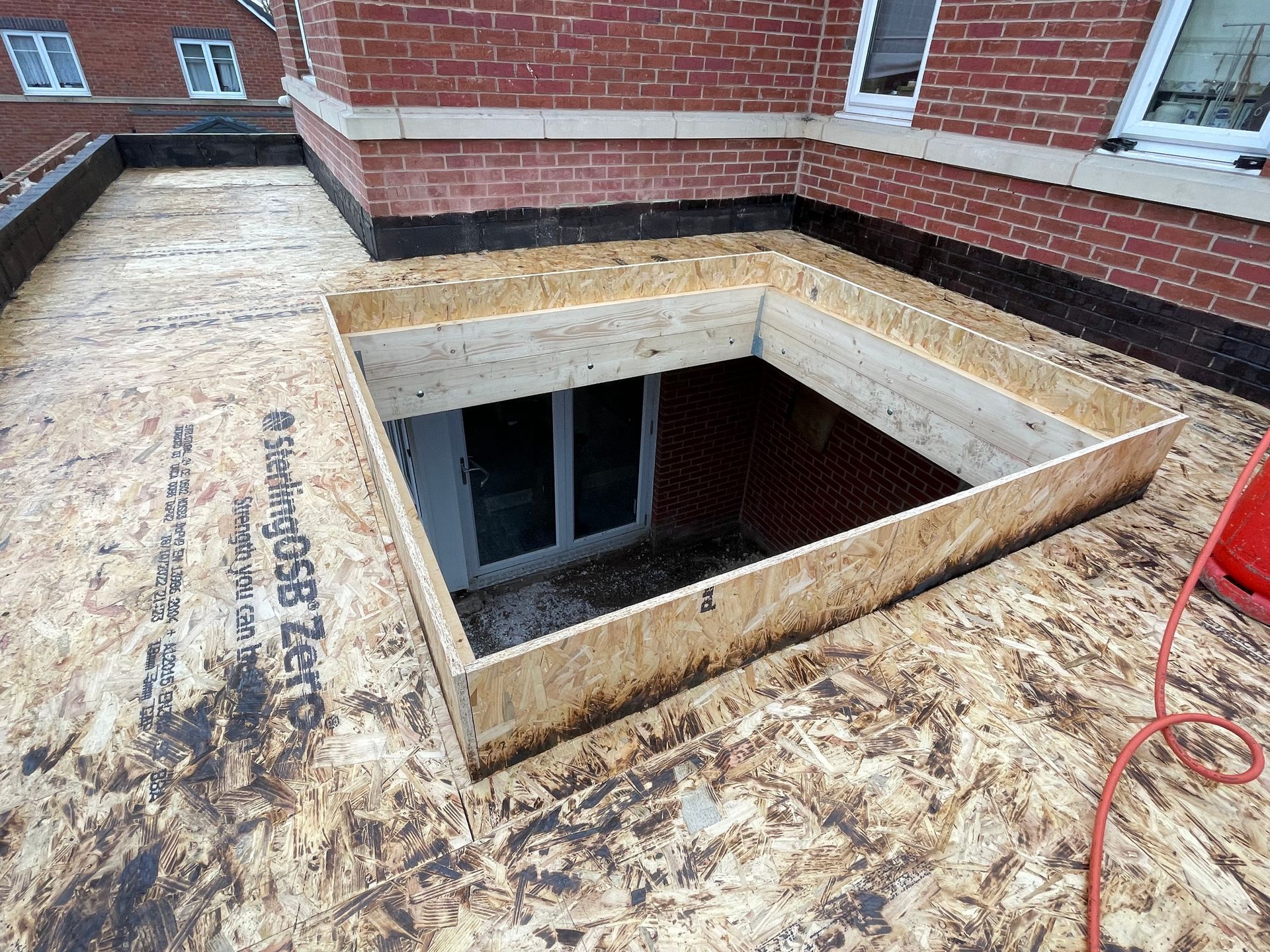 Rooftop construction: wooden frame around an opening to a door. Brick building in the background.