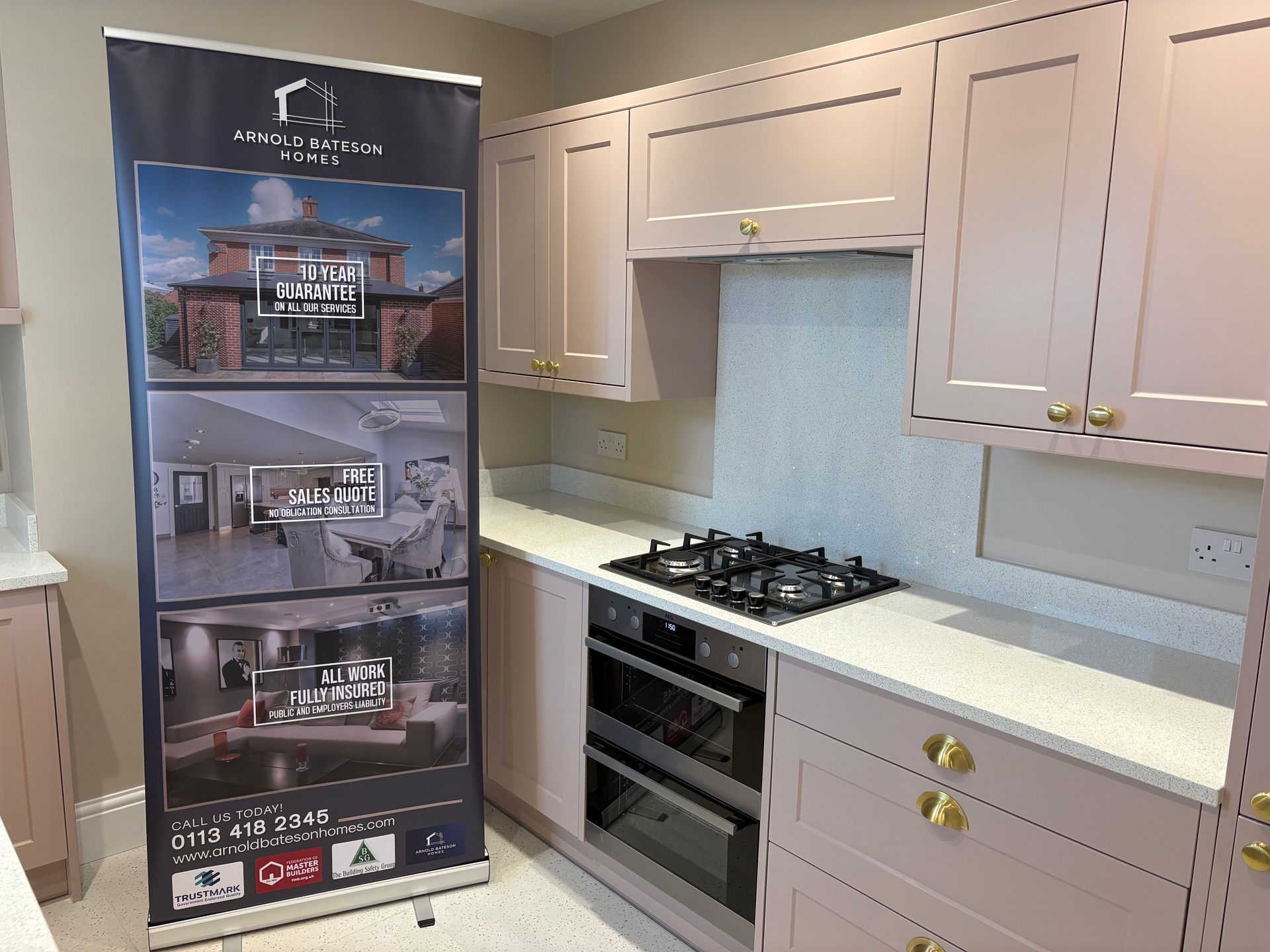 Kitchen with pink cabinets, white countertops, and a gas stovetop. A banner stands on the left.