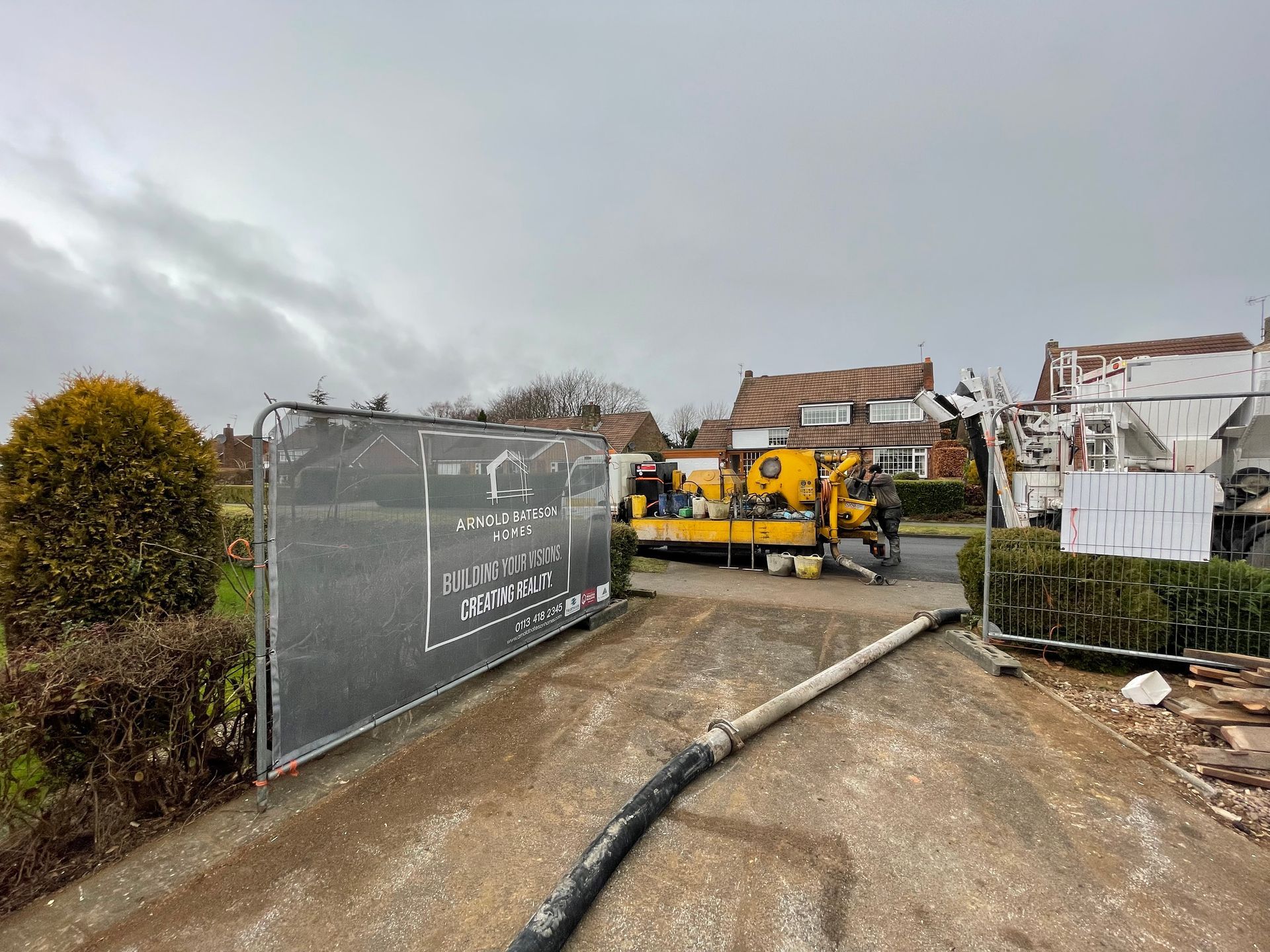 Construction site with a yellow pump machine, hose, and a fence. Cloudy sky.
