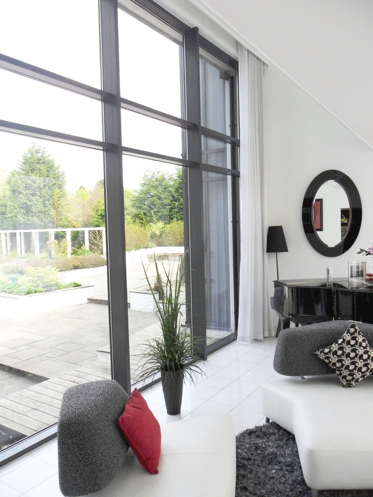 Modern living room with large windows, white walls, black furniture, and a view of the yard.