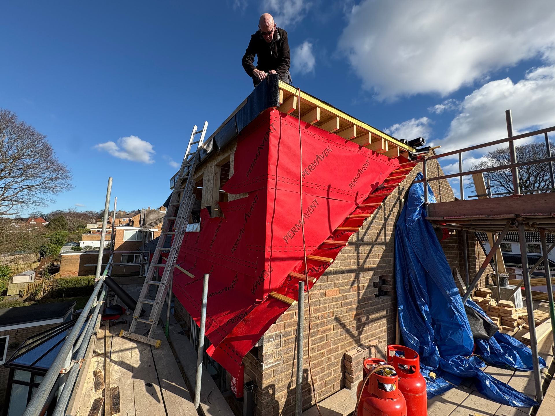 Man on a roof with red wrap, blue sky. Construction in progress.
