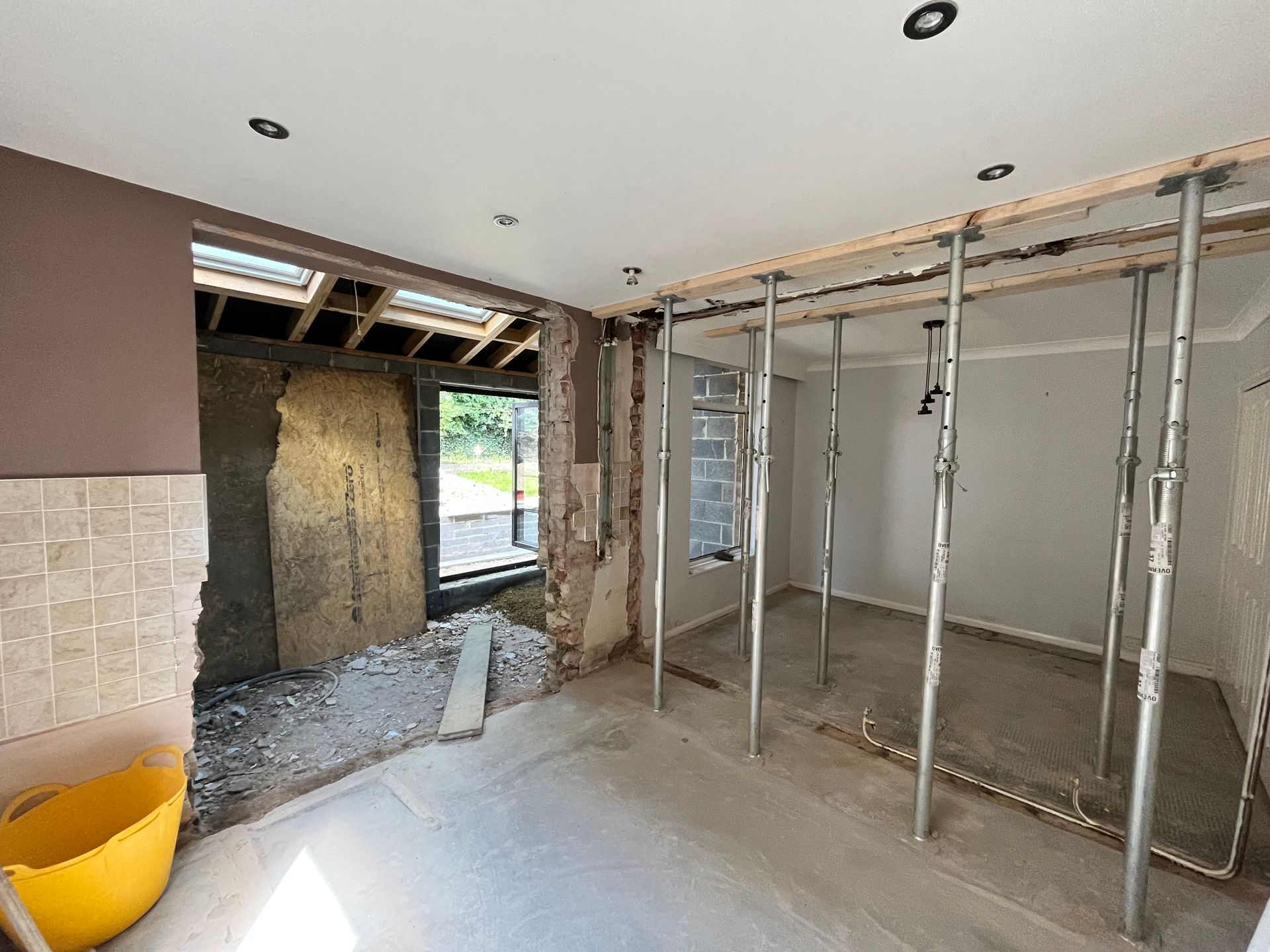 Interior room under renovation with support posts; doorway with exterior view.