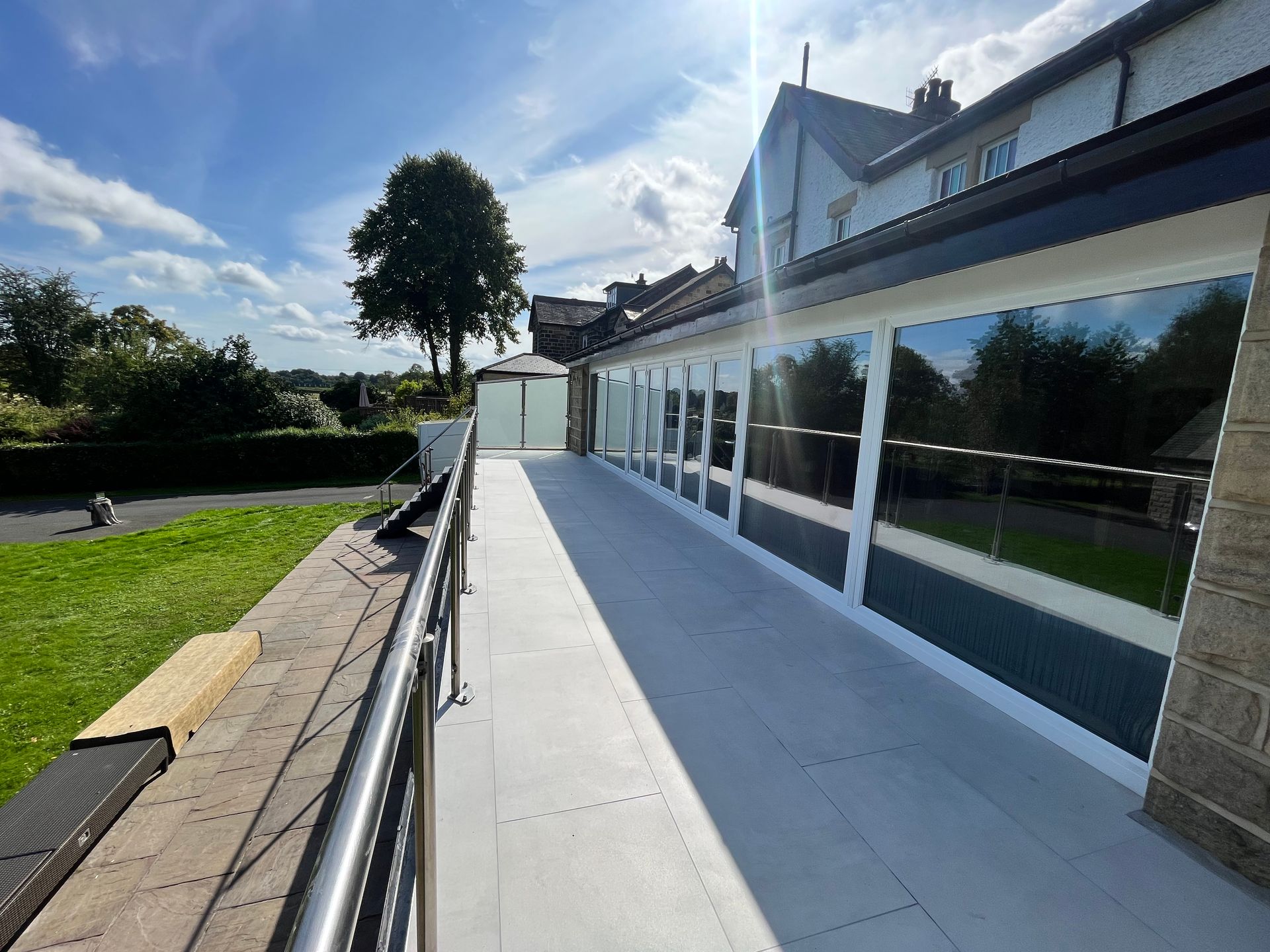 Ramp alongside a building with large windows. Stainless steel railing. Sunny day, blue sky, reflecting windows.