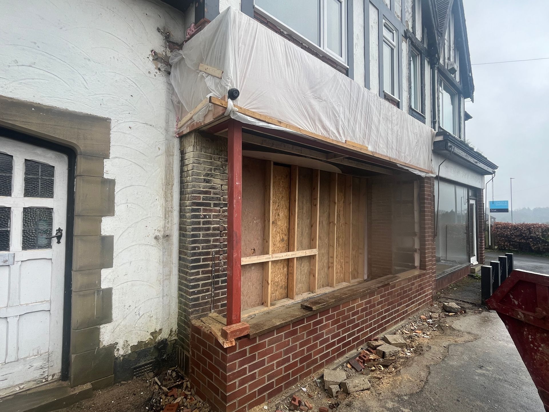Building exterior undergoing renovation; exposed brickwork, plywood, and protective sheeting.