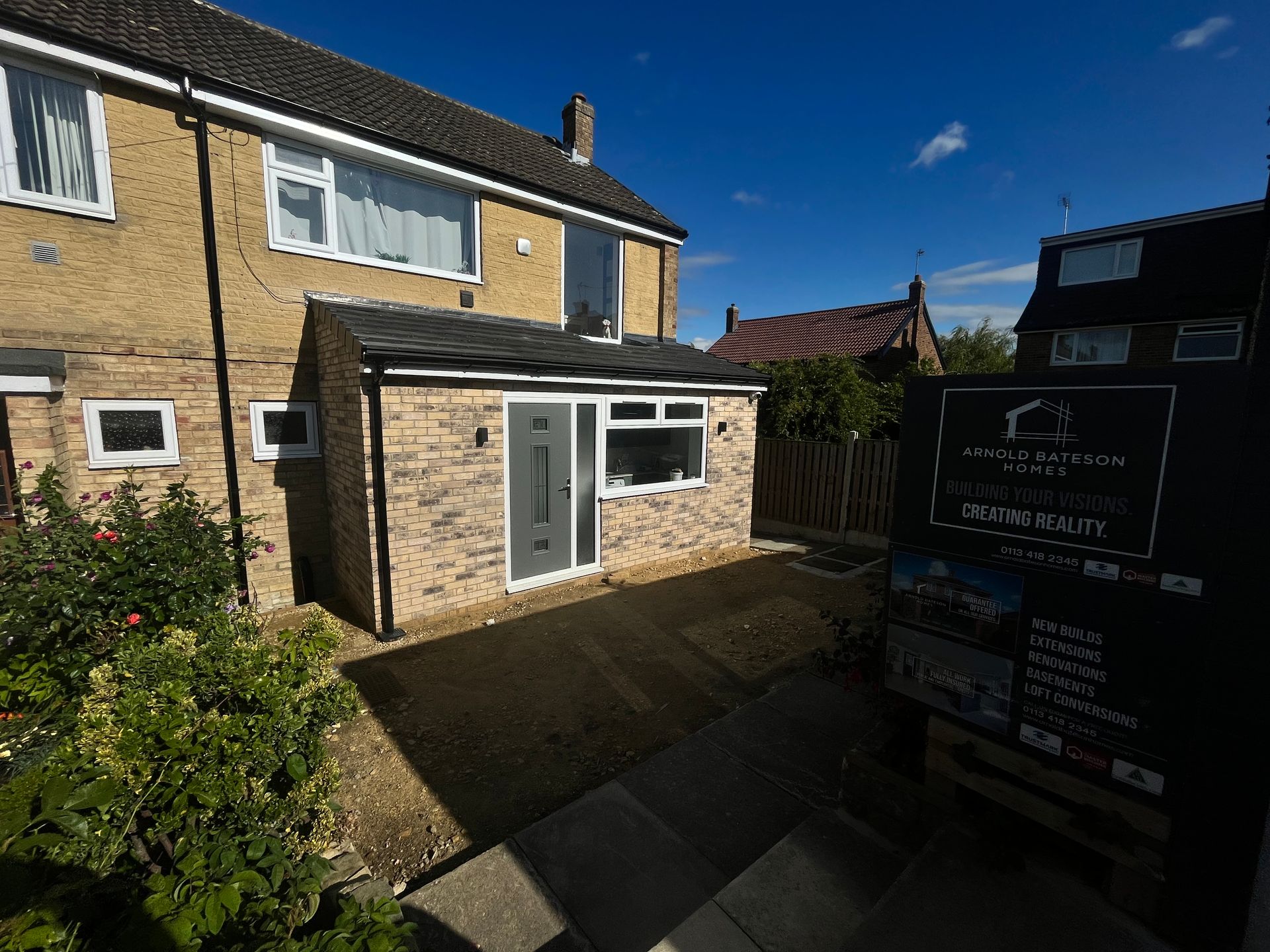 A brick extension with a grey door and window, attached to a house. A sign is in front.