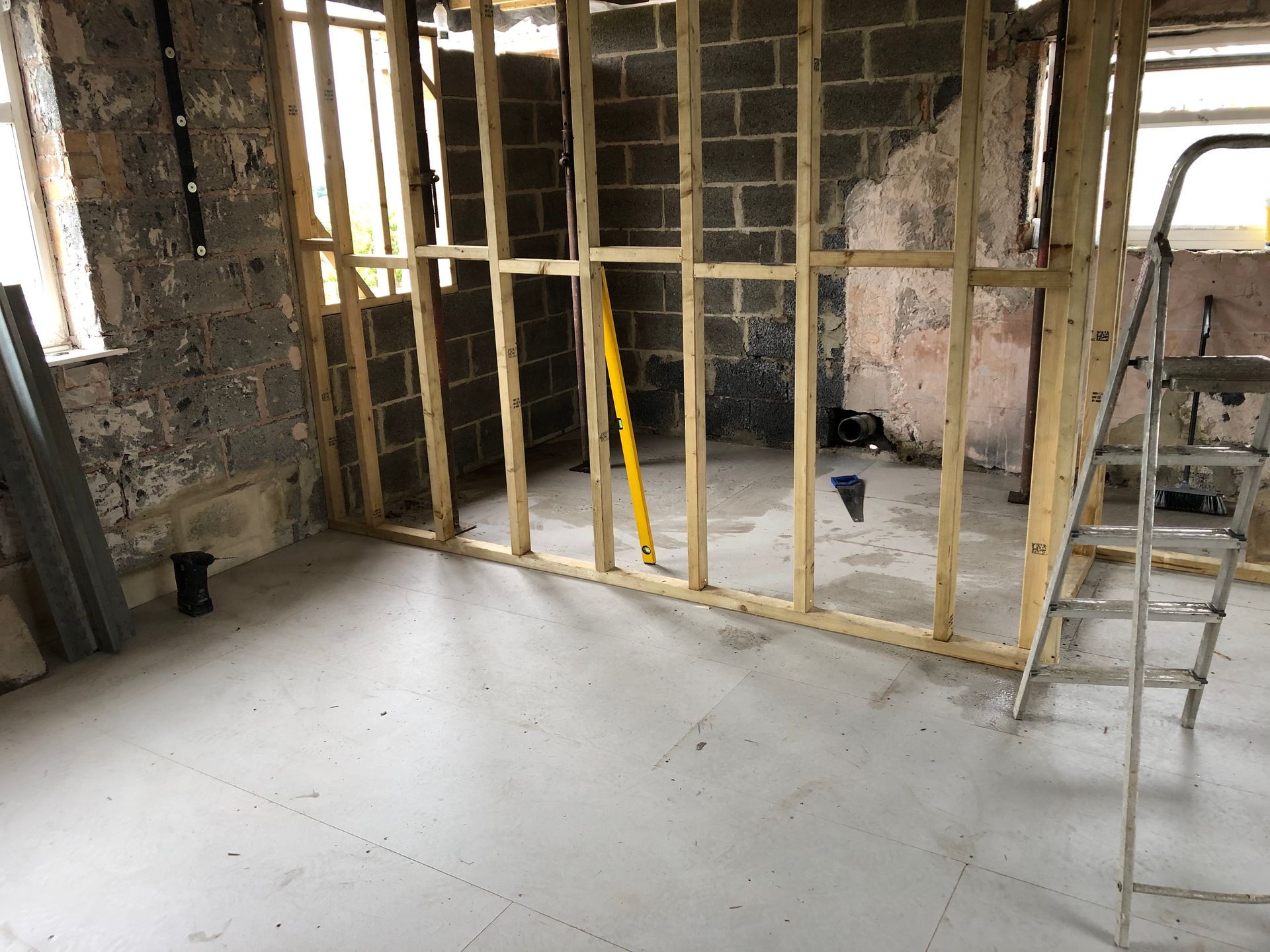 Room undergoing renovation: wooden frame, gray floor, cinder block wall, ladder, yellow level.