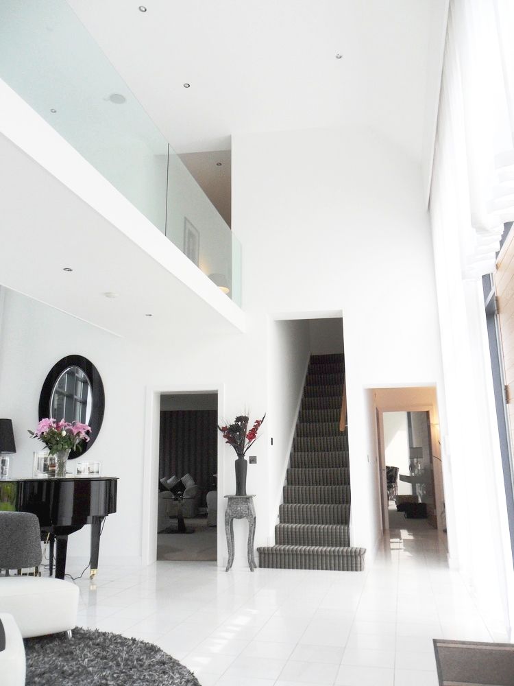 A modern, white-walled interior with a grand piano, staircase, and mezzanine.