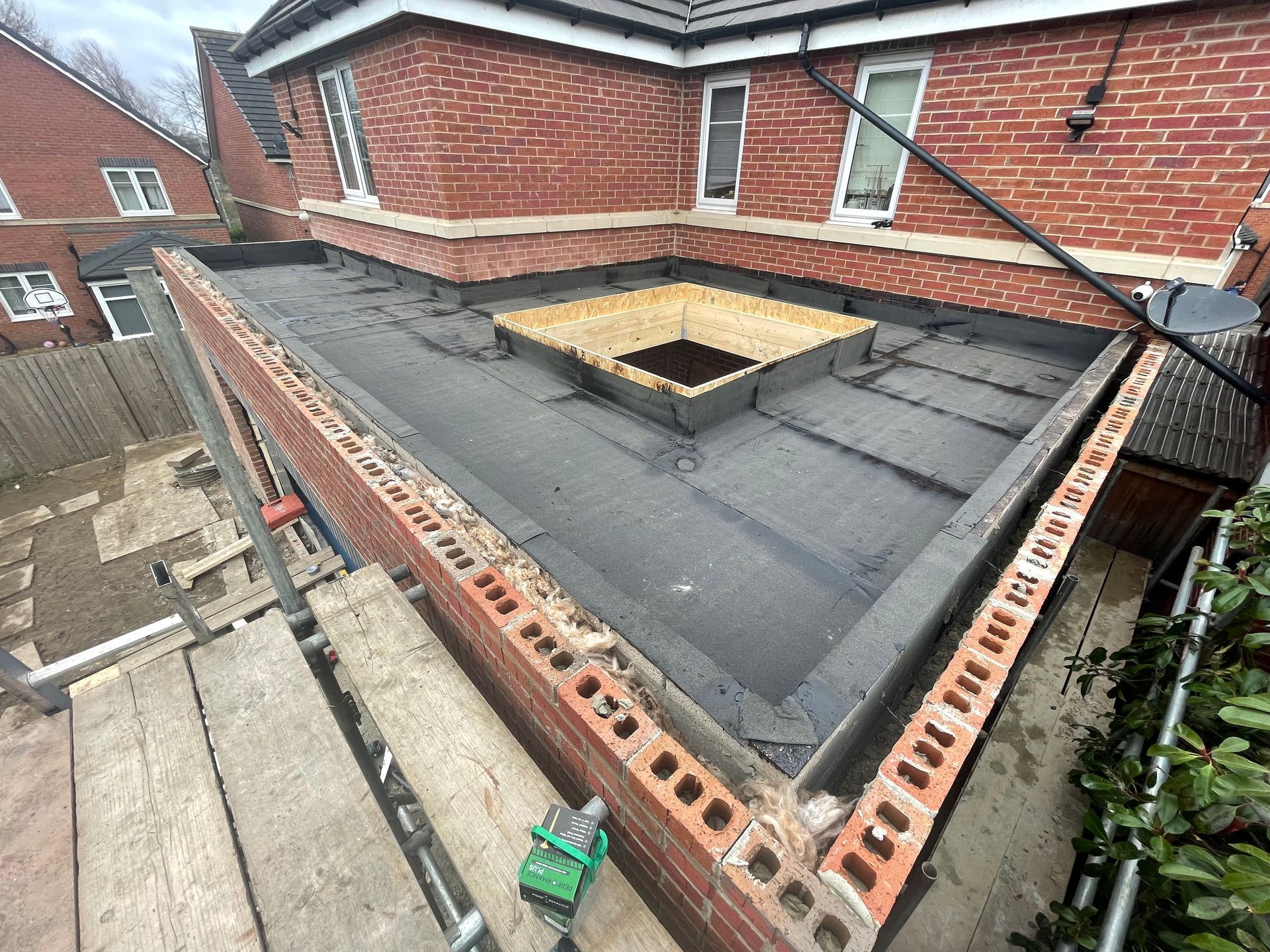 Flat roof with skylight under construction; red brickwork, black roofing, scaffolding.