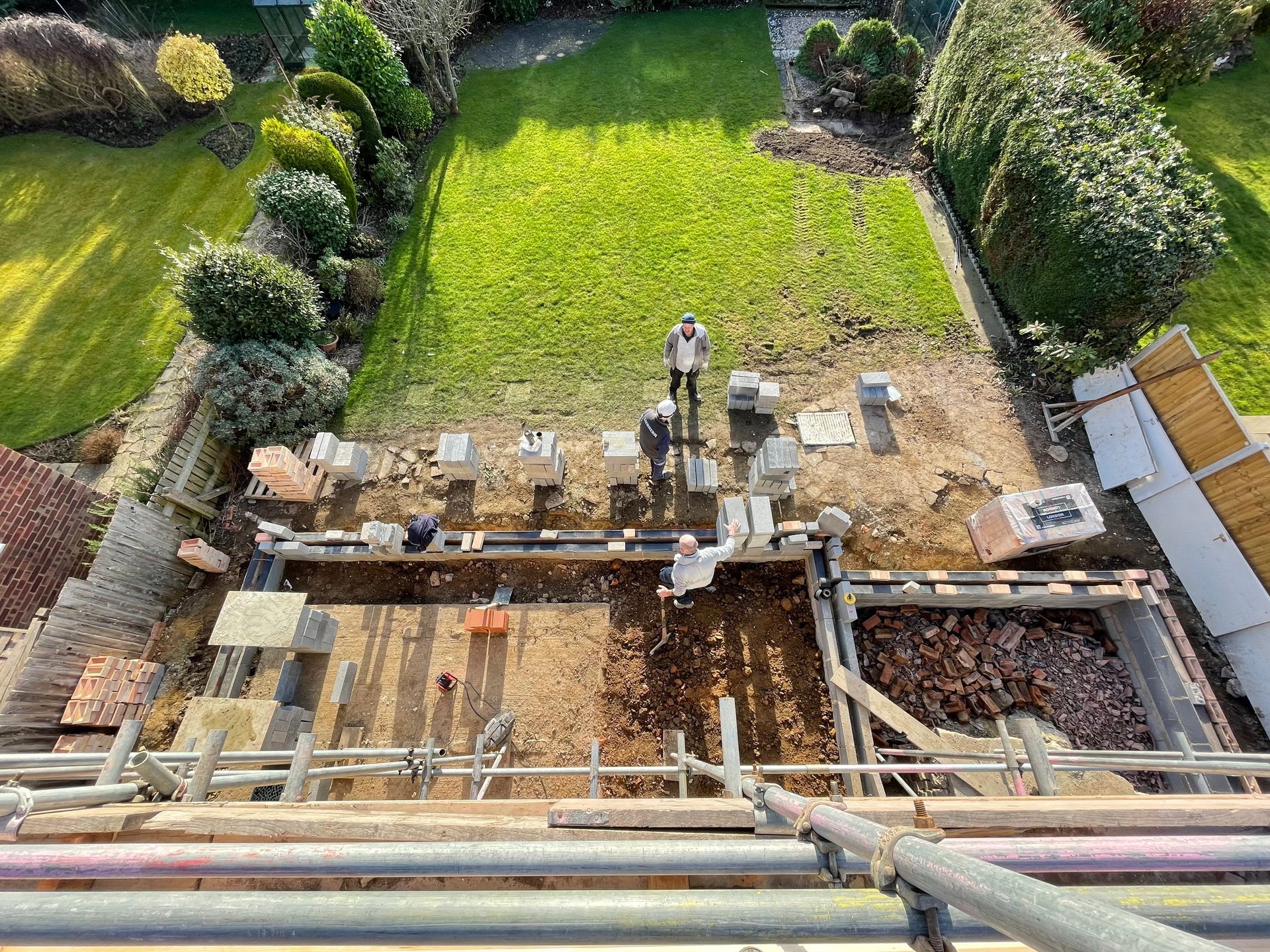 Construction workers building a structure outdoors, with a backyard and green lawn visible.