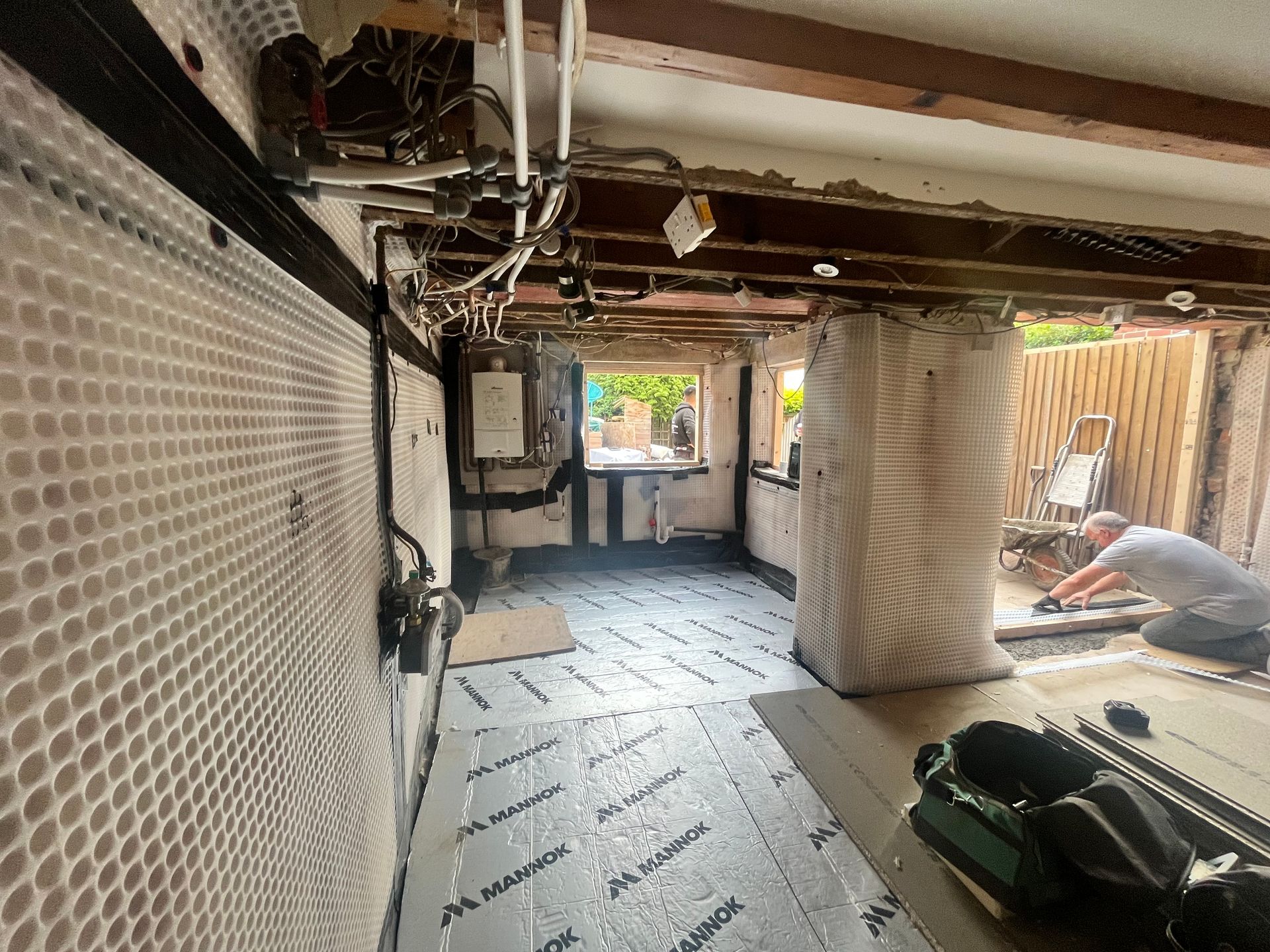 Room under renovation with exposed beams, insulation, and a worker installing flooring.
