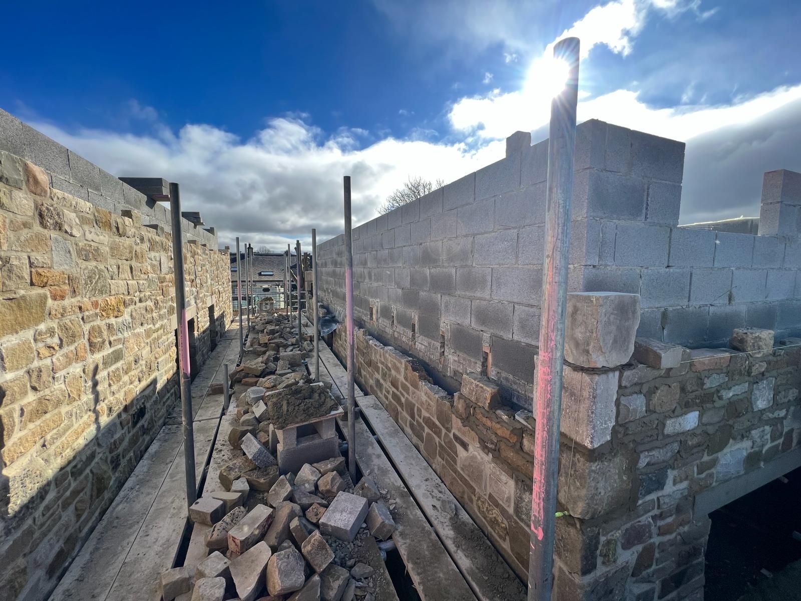 Construction site with stone walls and rubble under a bright blue sky.