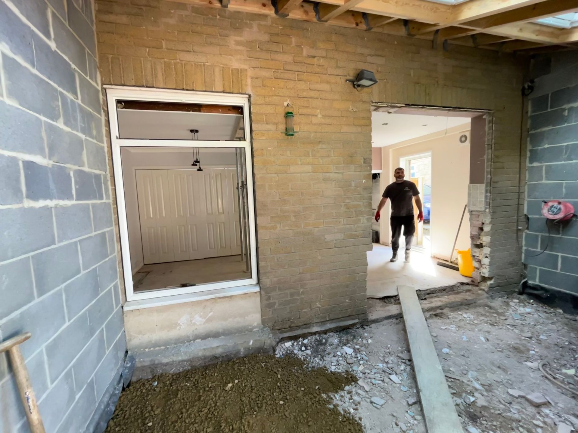 Construction site with a person walking through doorway, connecting to a room with light colored walls.