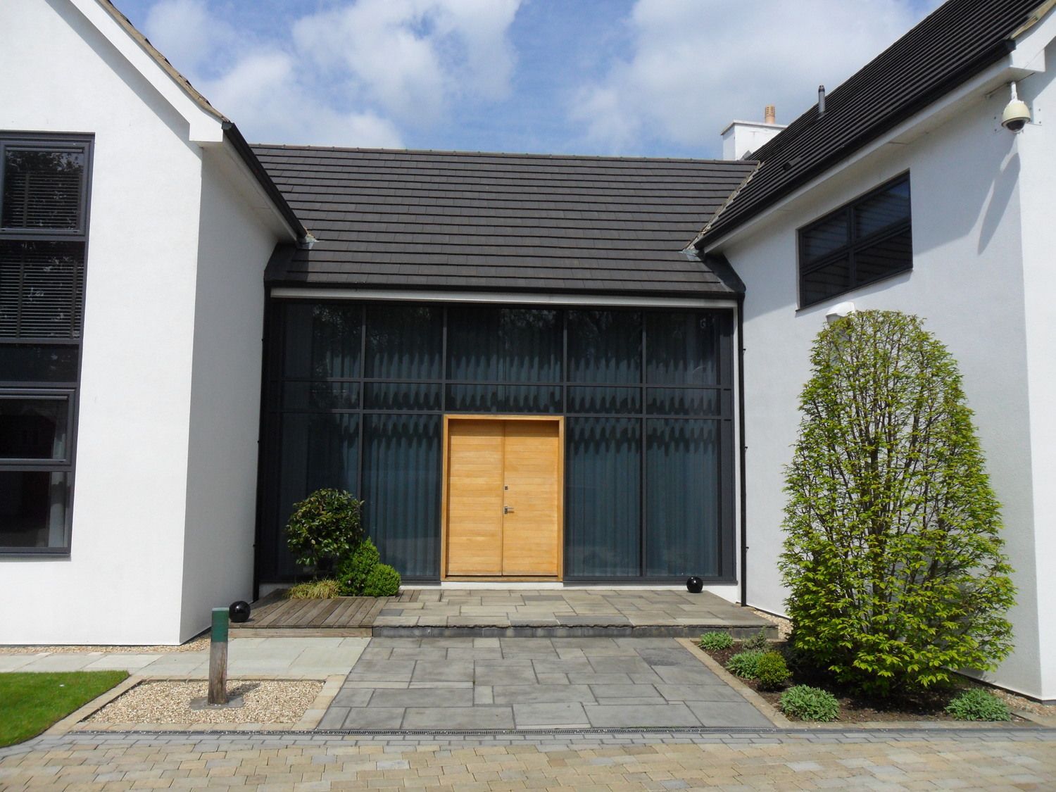 Modern house entrance with wooden door, glass panels, and gray stone pathway.