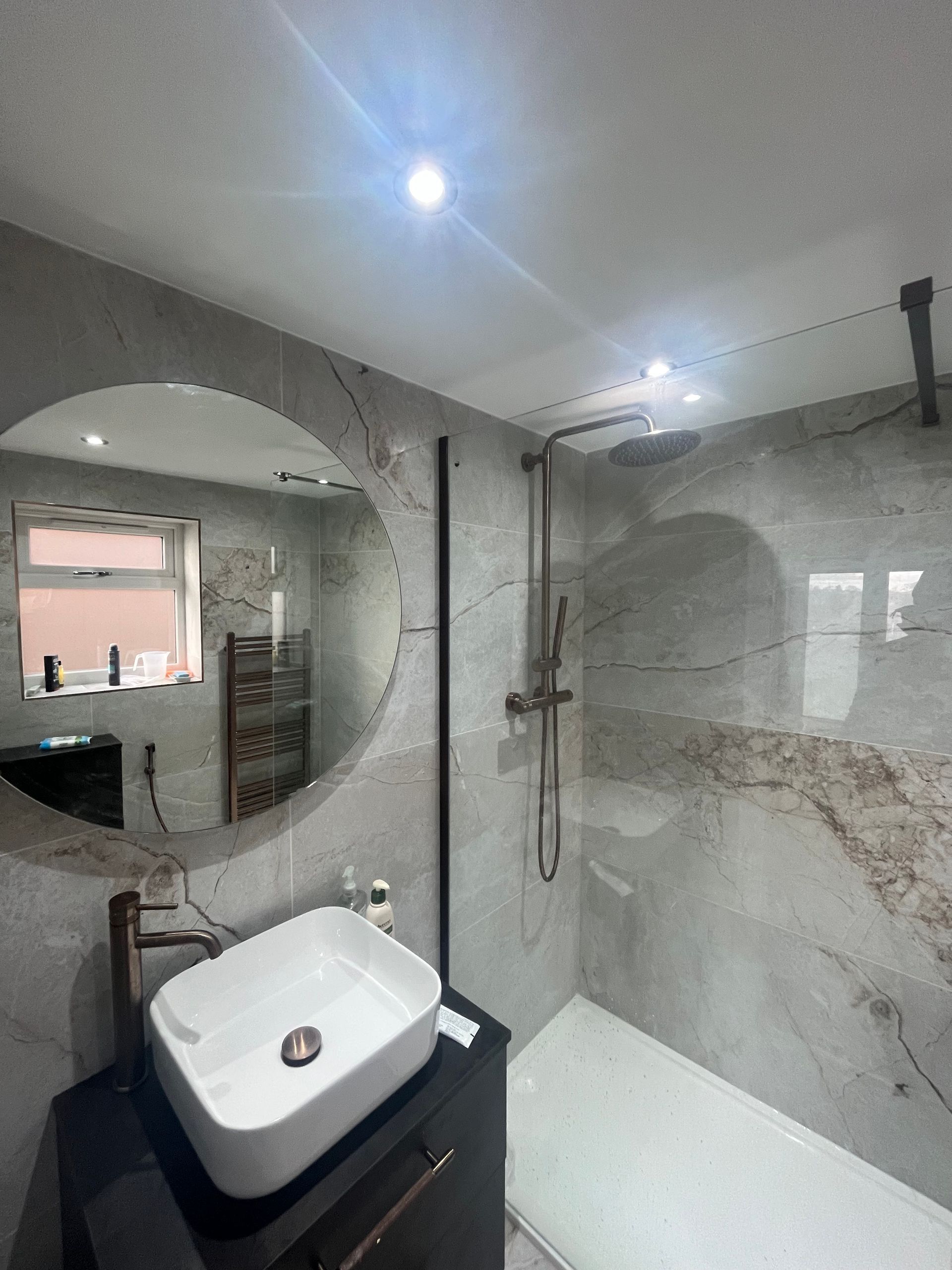 Modern bathroom with marble-look tiles, a circular mirror, and a sleek white sink.