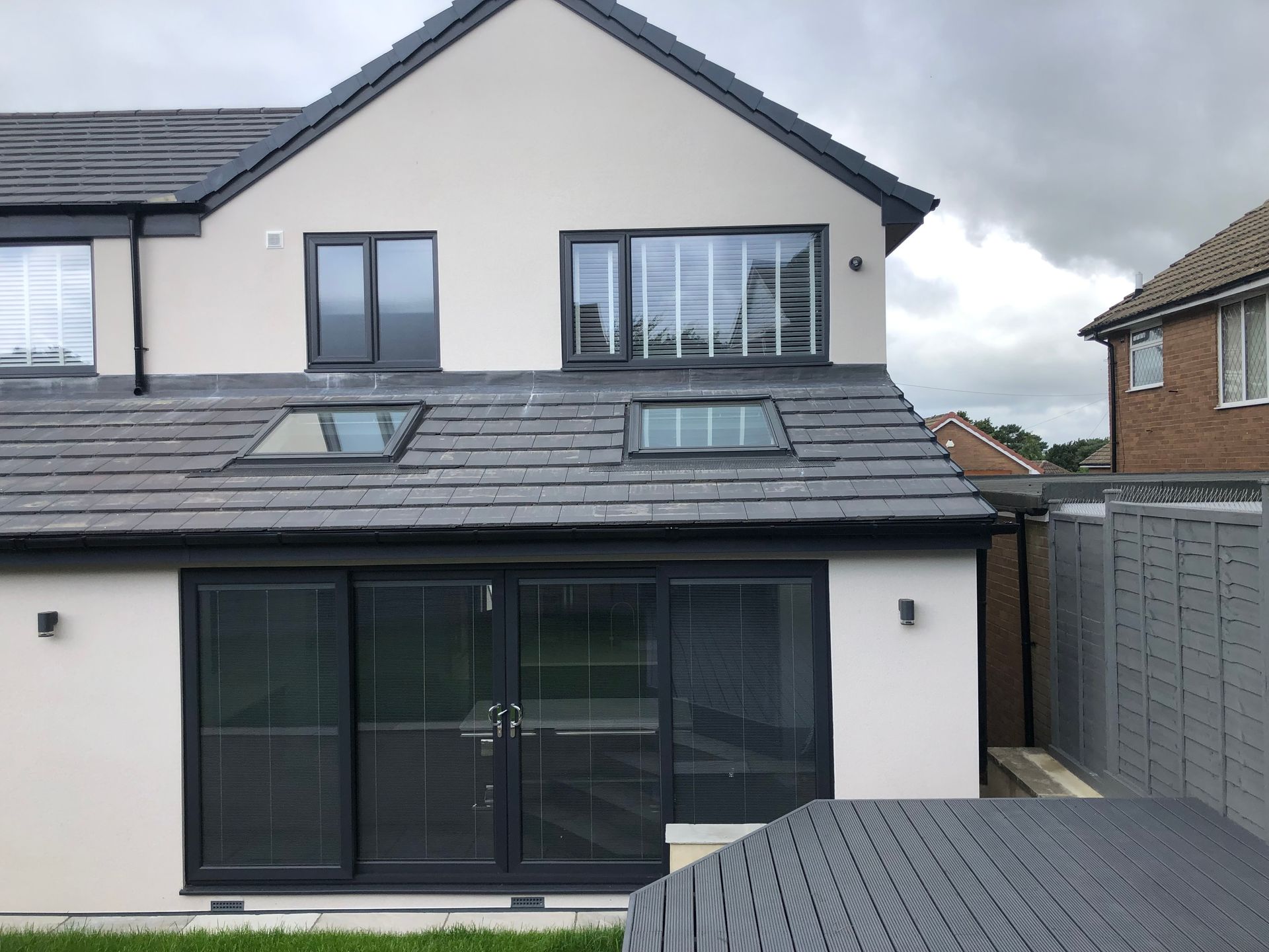 Back of a modern house with gray roof, white walls, and dark gray window frames and doors.