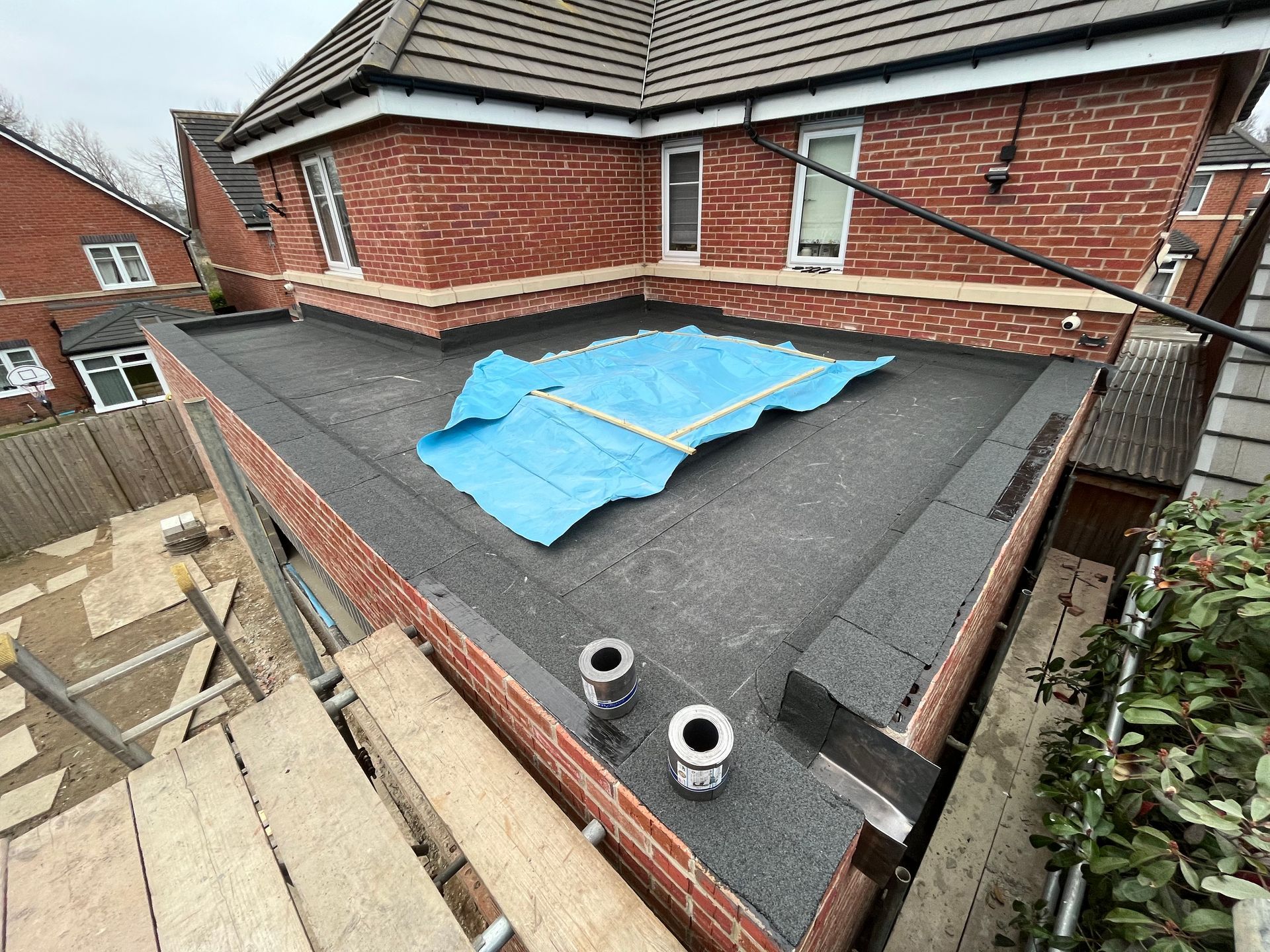 Flat roof under construction with brick building, scaffolding, and blue tarp.