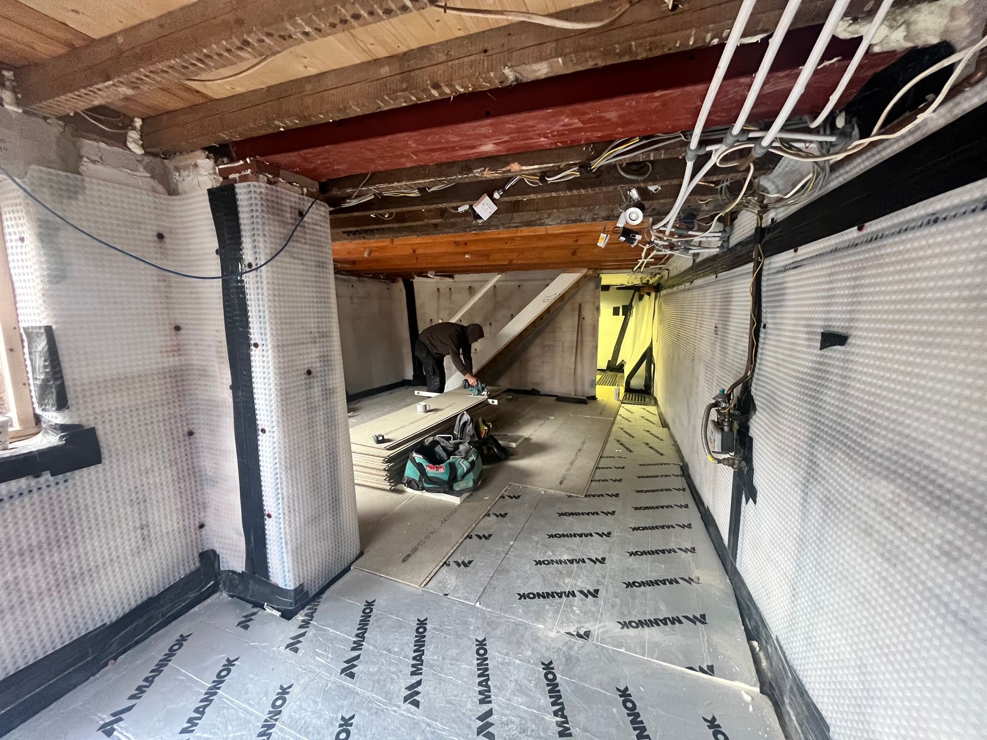 Basement renovation in progress, with worker, insulation, and vapor barrier visible.