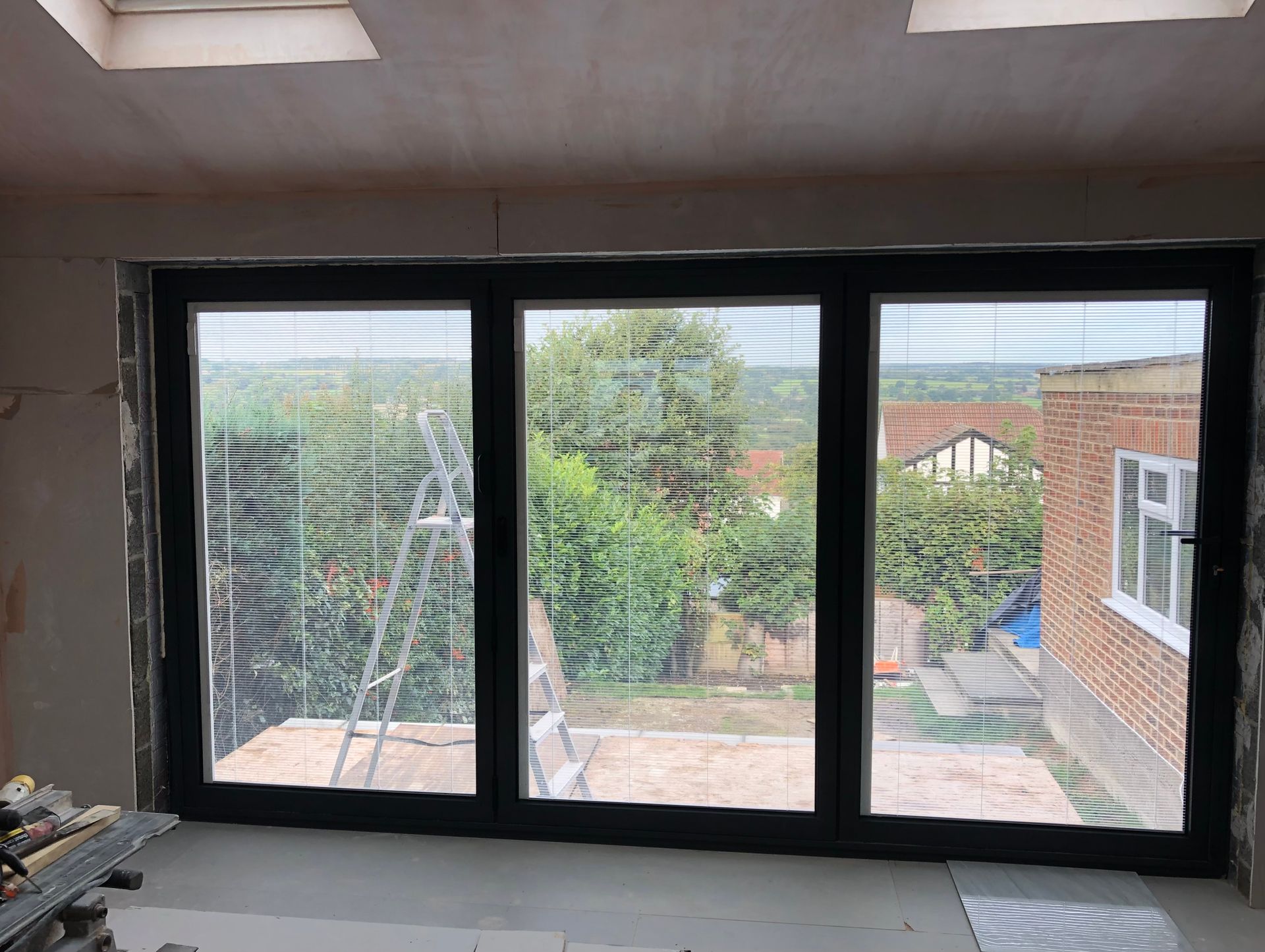 Interior view with new black framed, three-panel glass door overlooking a yard and houses under construction.