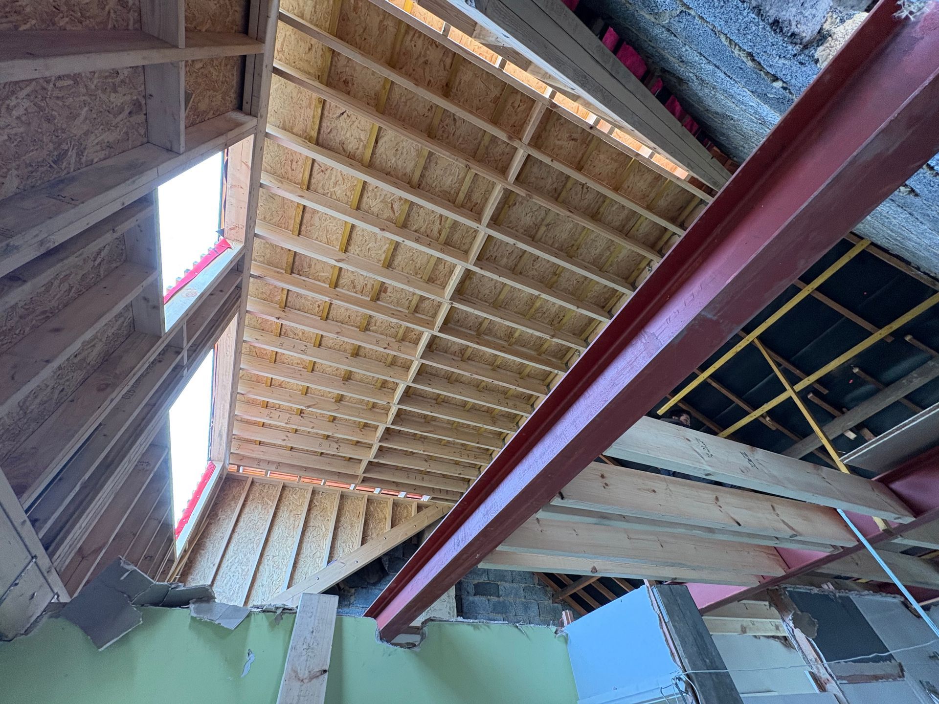 Interior of a building under construction. Red steel beam supports a wood ceiling with skylights.
