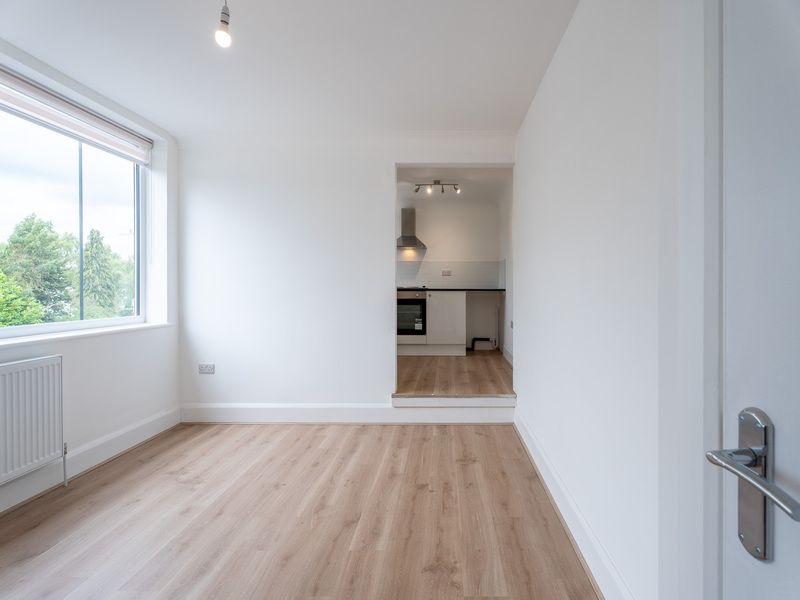 Empty room with light wood floors, a window, and a glimpse of a kitchen.