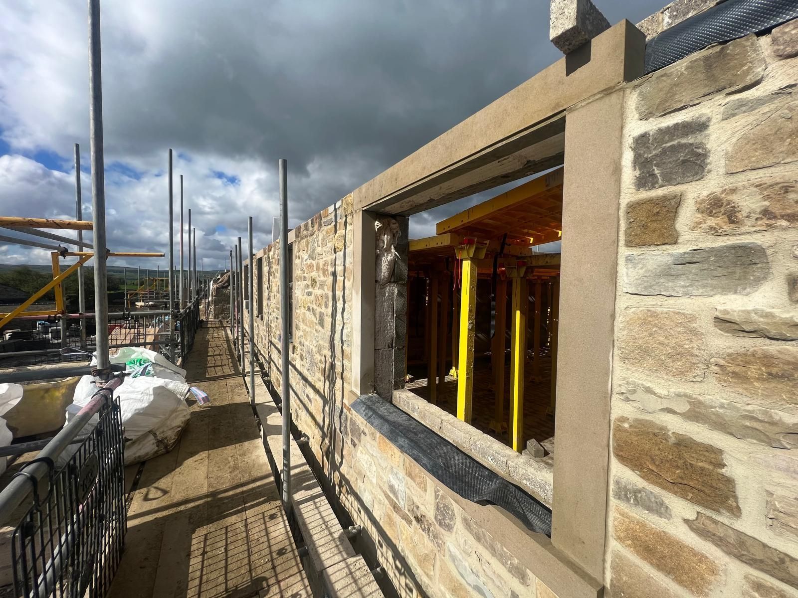 Stone building under construction, with scaffolding. Window frames, cloudy sky.