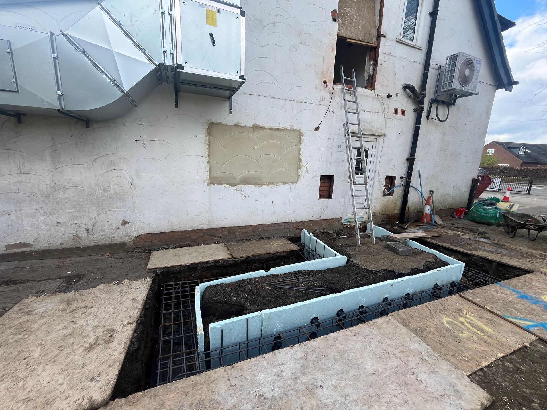 Exterior building under construction with exposed foundation and ventilation duct.