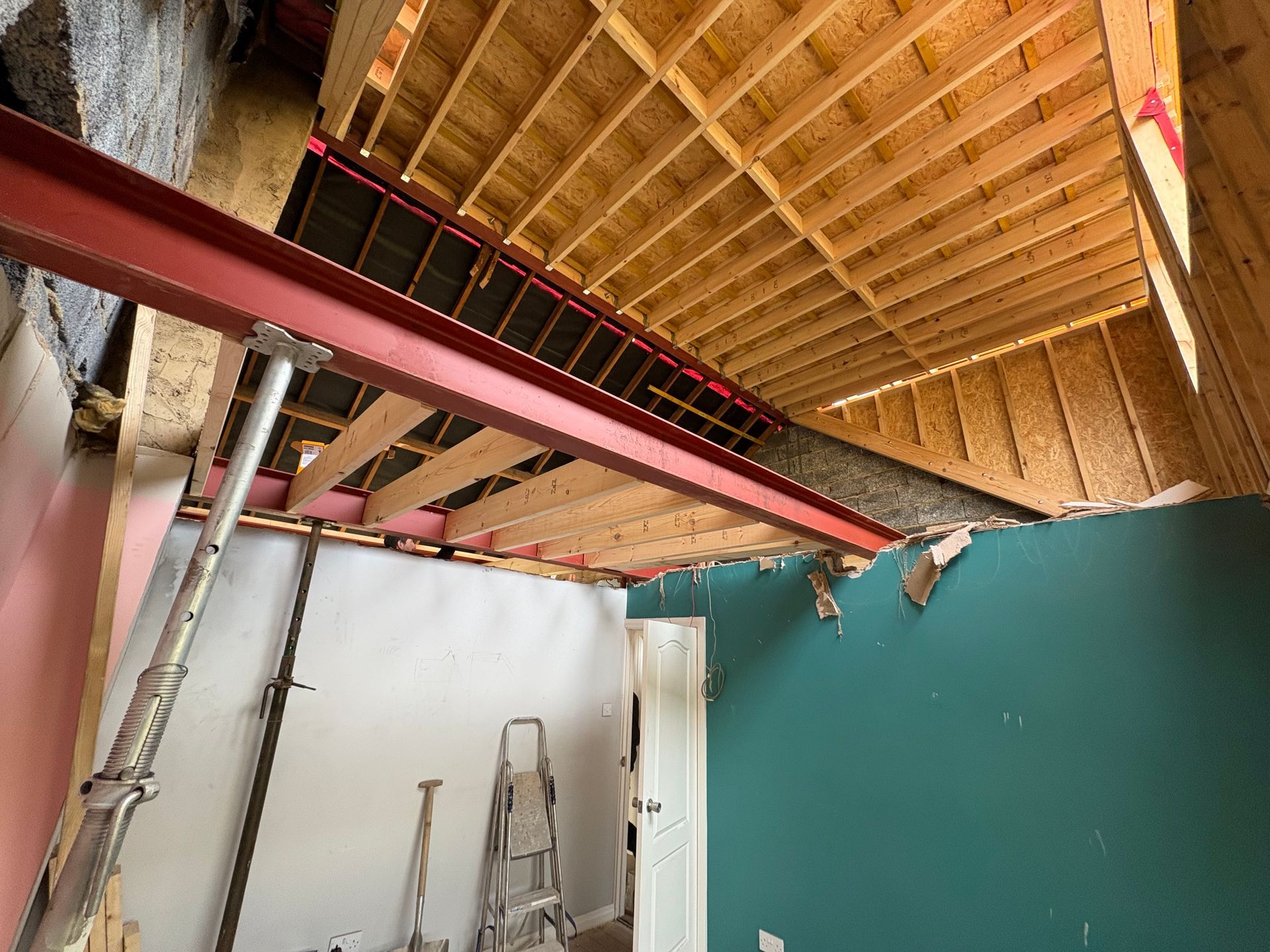 Red steel beam supports ceiling under construction; room with teal wall.