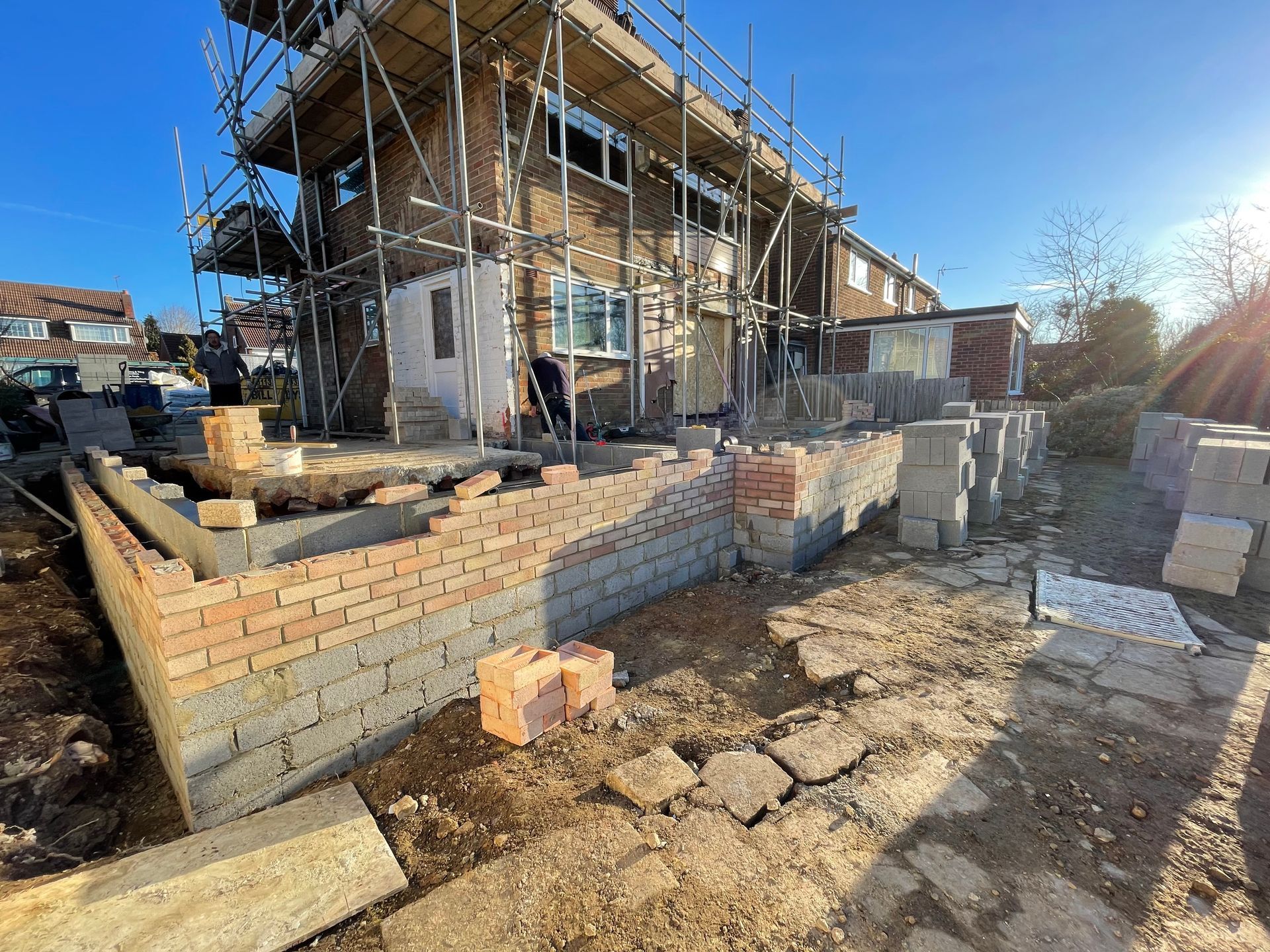 Construction site with a two-story brick house under renovation, scaffolding, and foundation work.