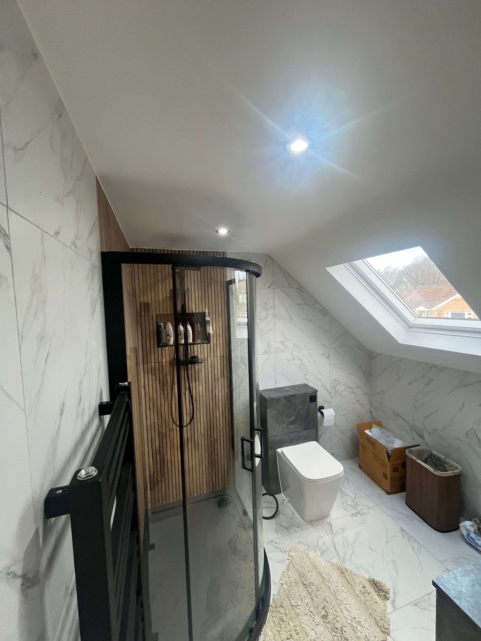 Modern bathroom with slanted ceiling. Shower, toilet, and window. White and wood tones.