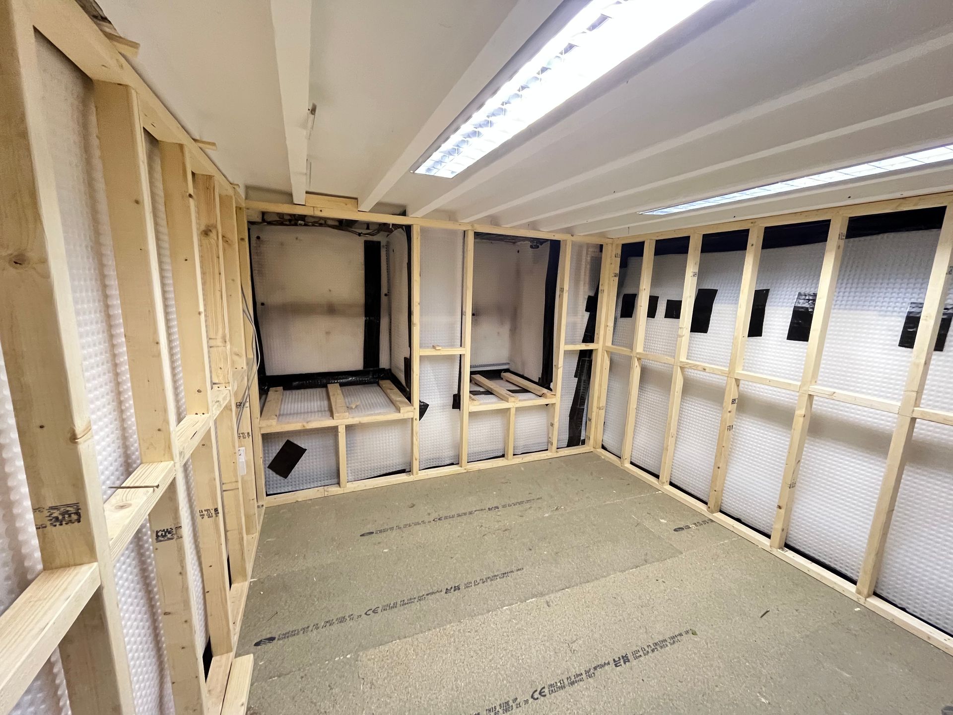 Interior room under construction: wooden frame walls, insulation, and exposed ceiling.