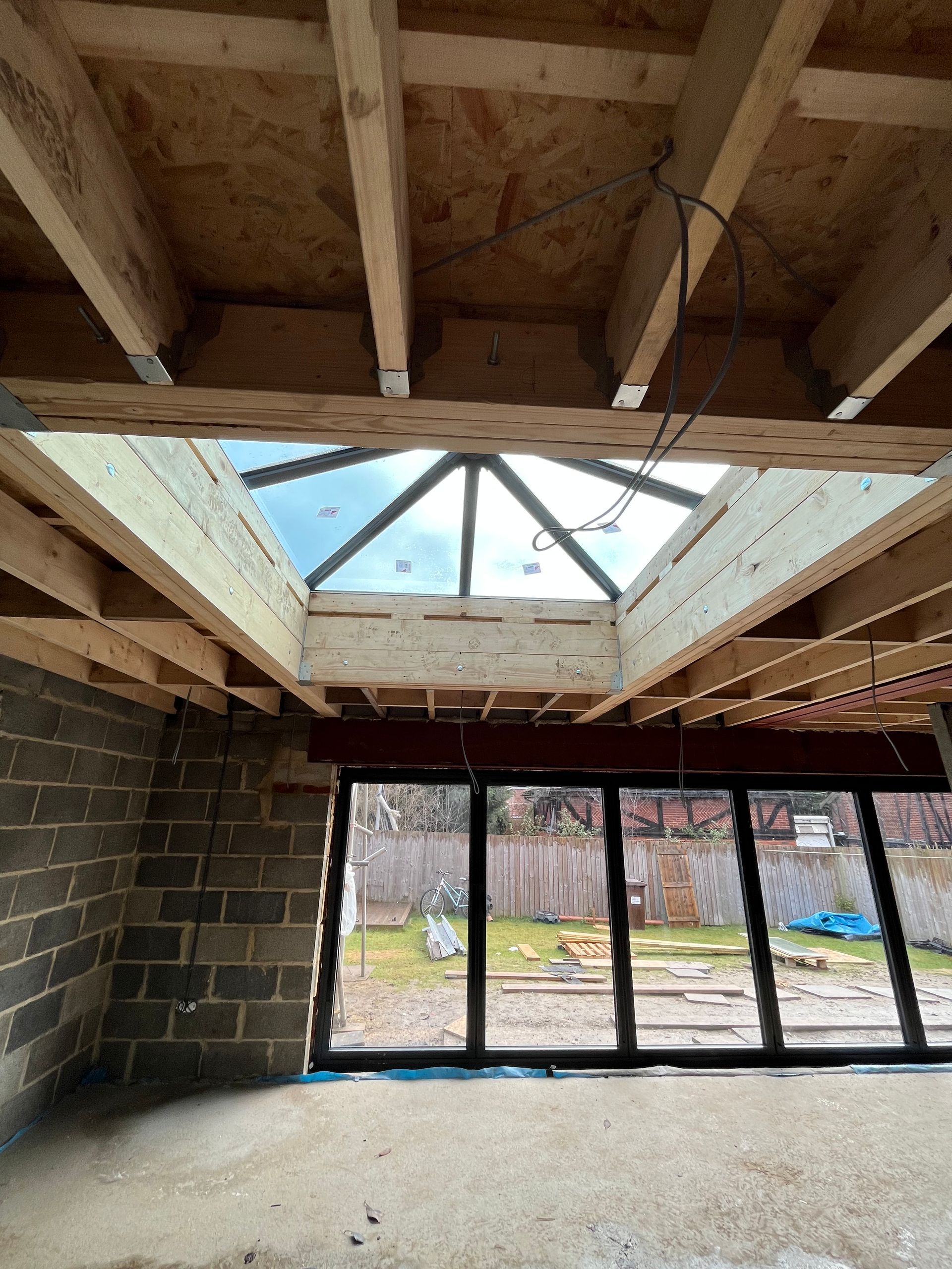 Interior under construction with a skylight, brick wall, and large glass doors leading to a backyard.