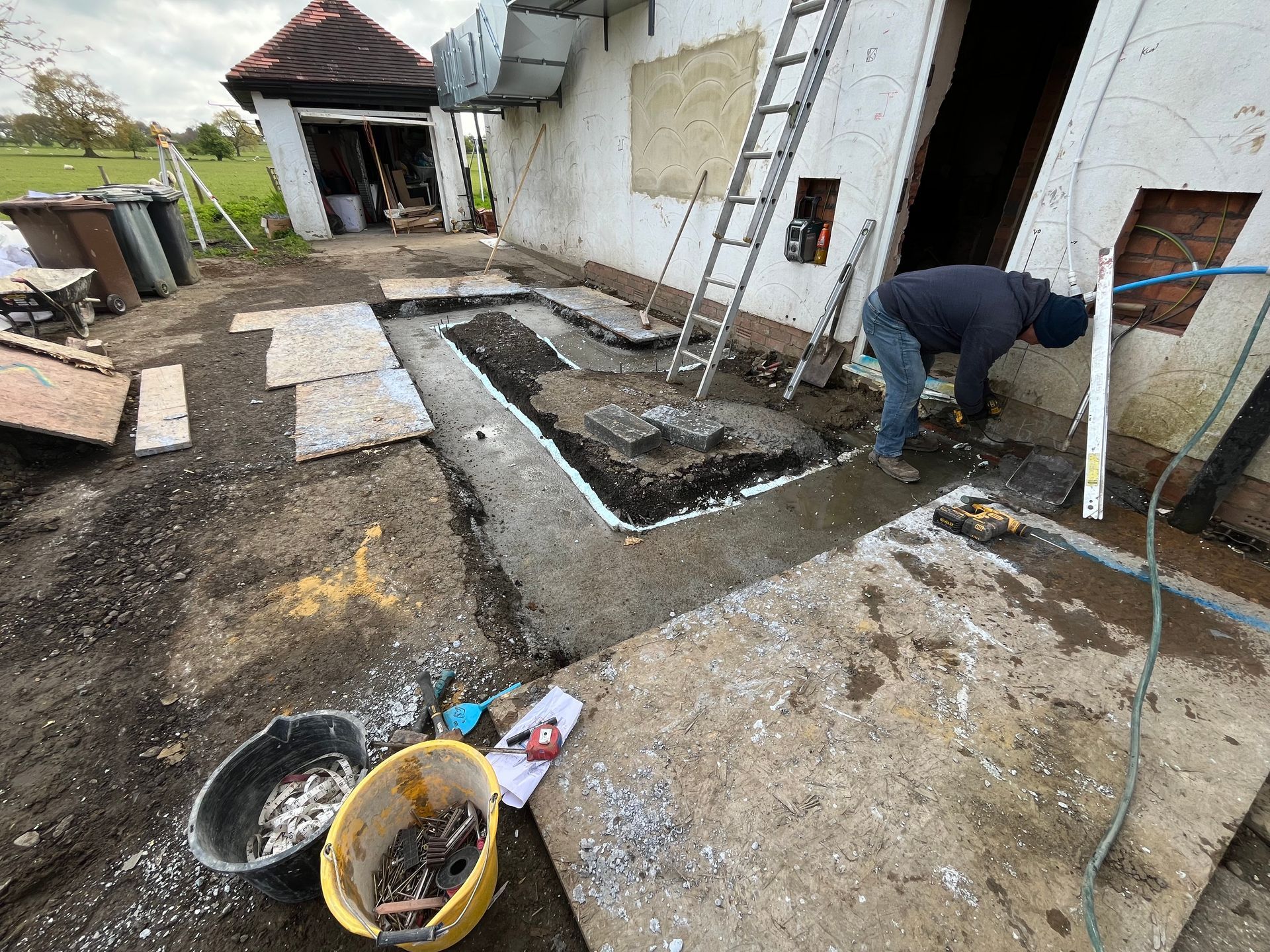 Construction worker working on a concrete foundation outside a building. Tools and debris scattered around the site.