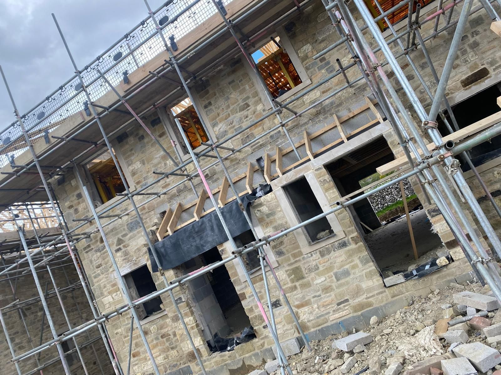 Exterior of a building under construction, scaffolding around stone walls, multiple window openings.