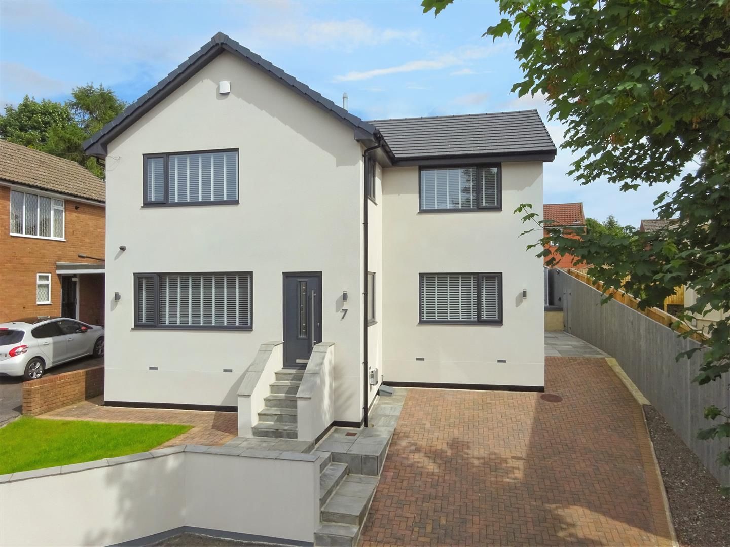 Modern white house with dark gray windows and door, front steps, and driveway.