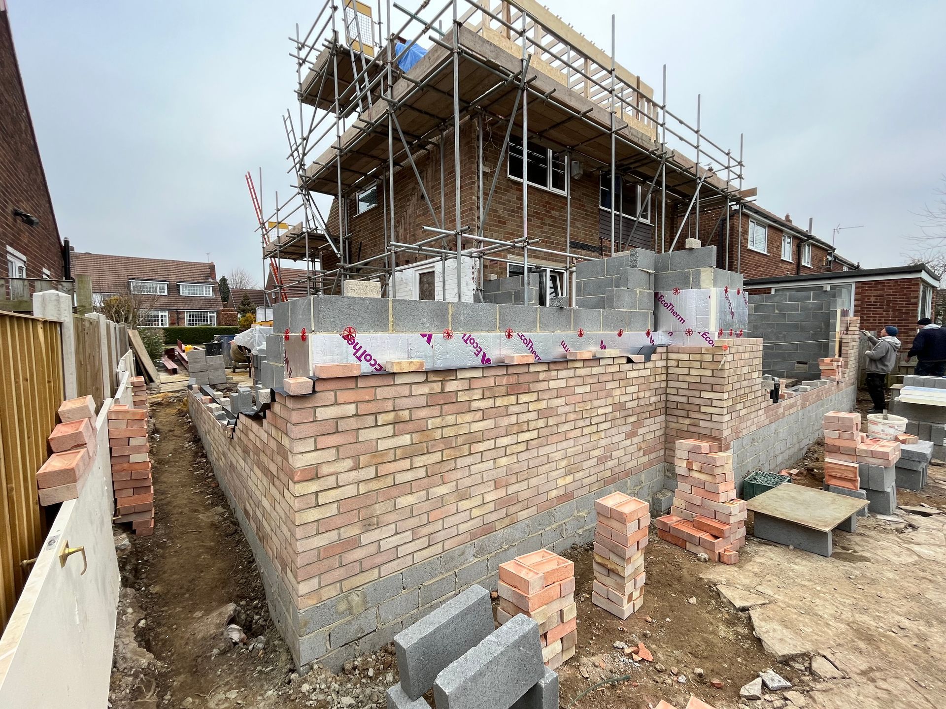 Construction site with bricklaying, scaffolding, and a two-story house under renovation.