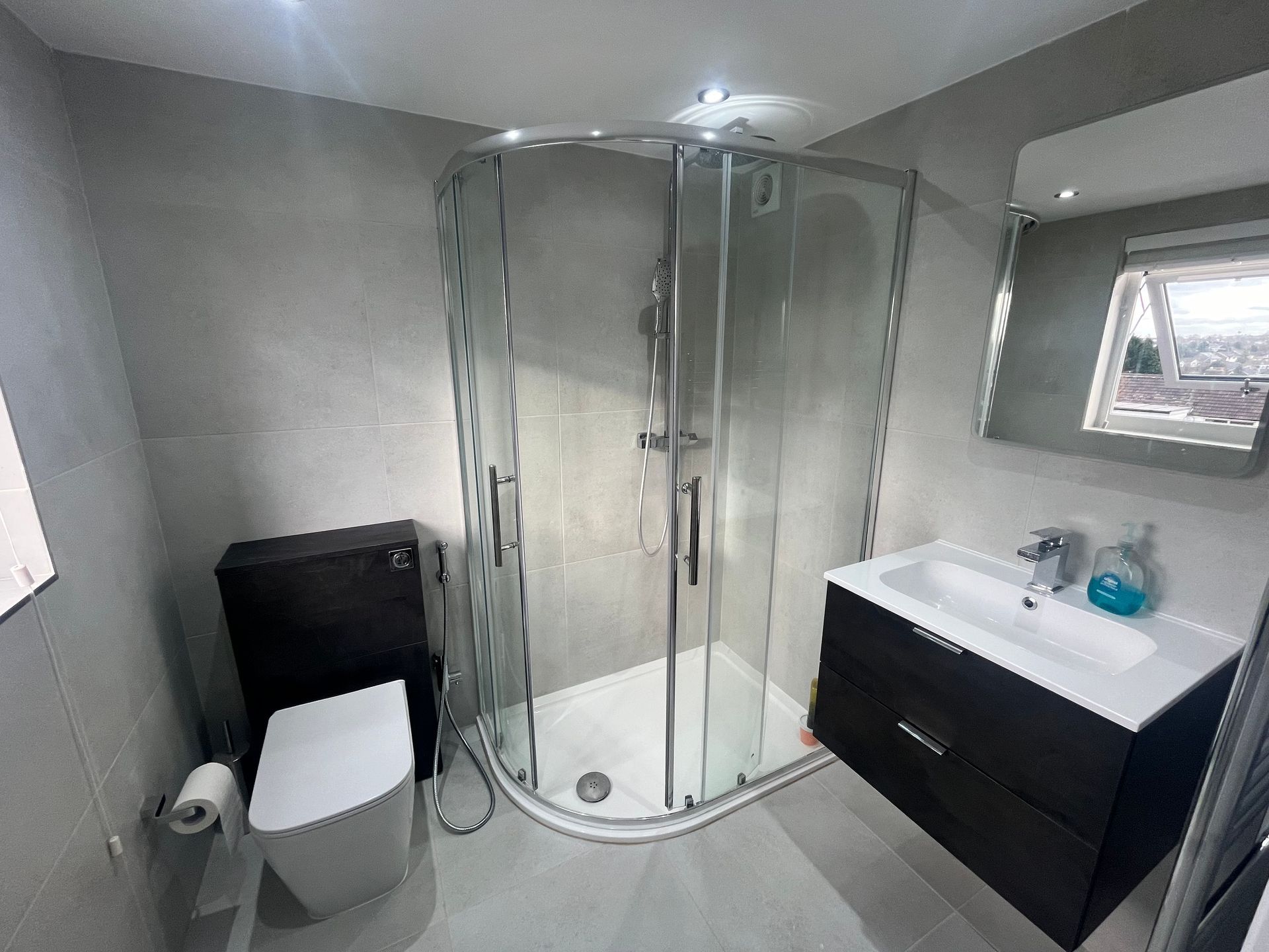 Bathroom with a corner shower, toilet, sink, and mirror. Gray walls, dark cabinet, and white fixtures.