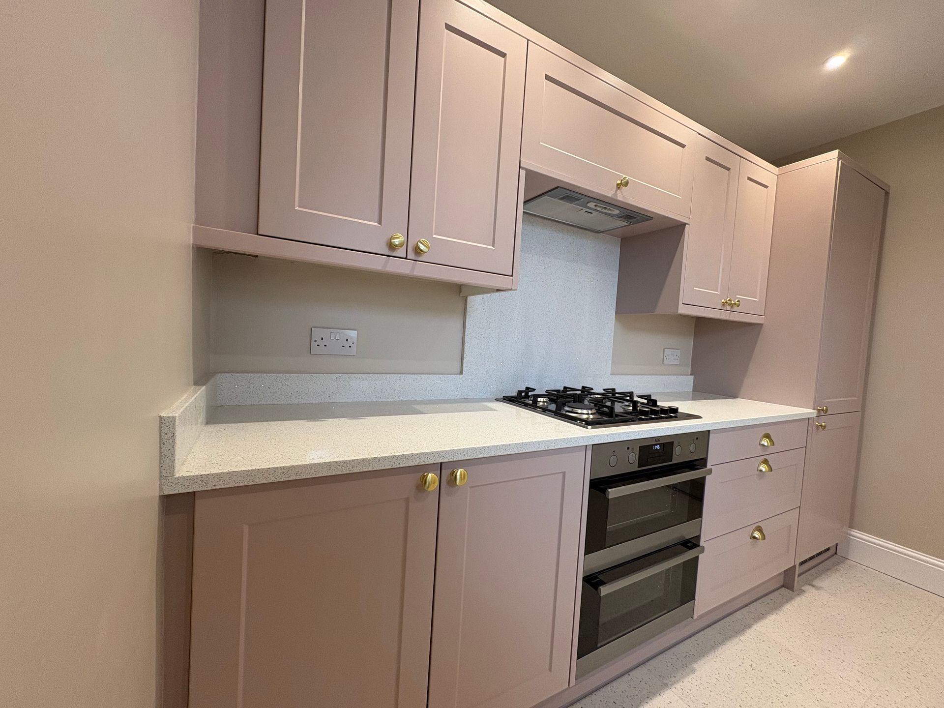 A kitchen with pink cabinets, gold hardware, and white countertops. Includes a gas stove and double ovens.